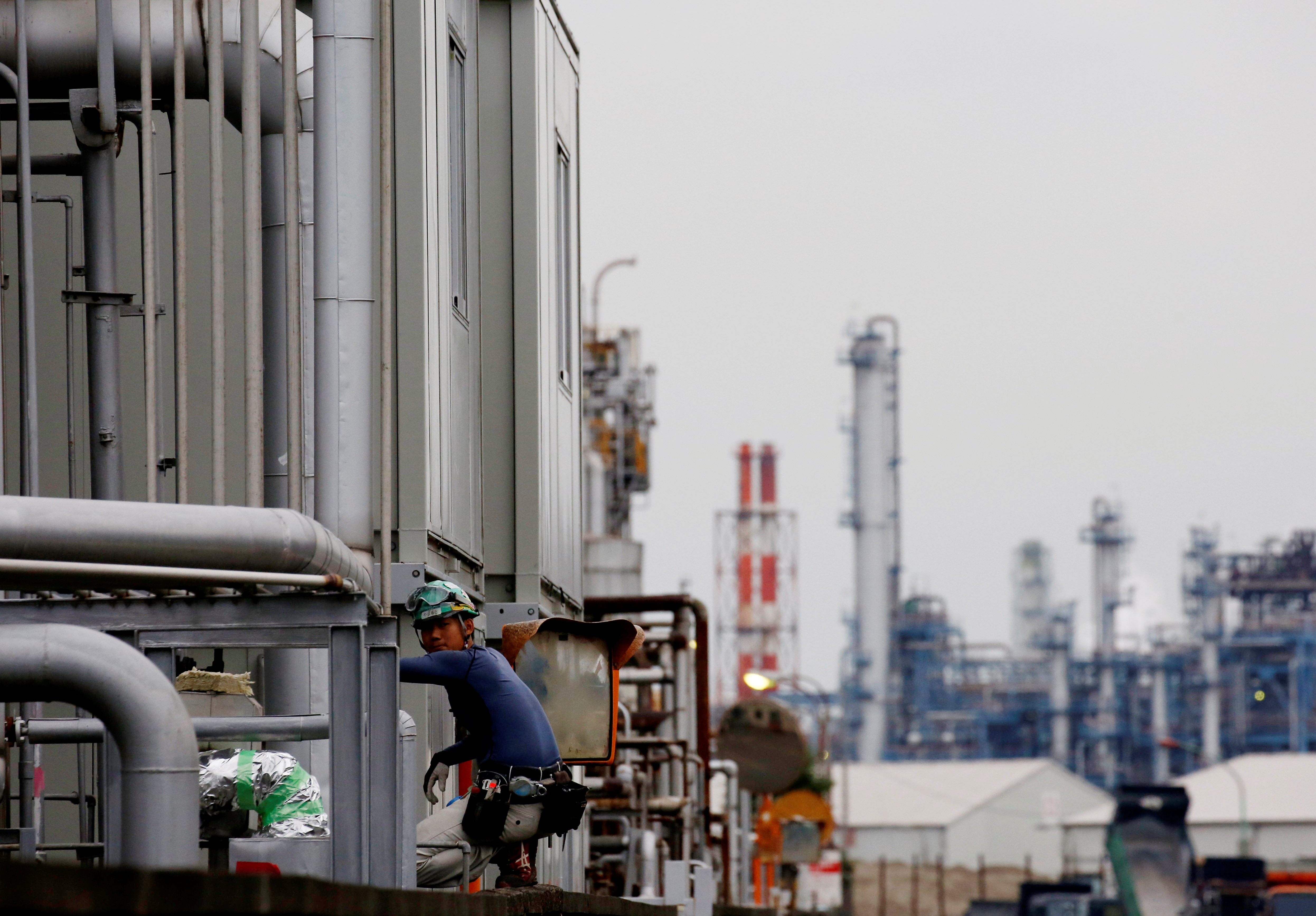 A worker is seen in front of facilities and chimneys of factories at the Keihin Industrial Zone in Kawasaki
