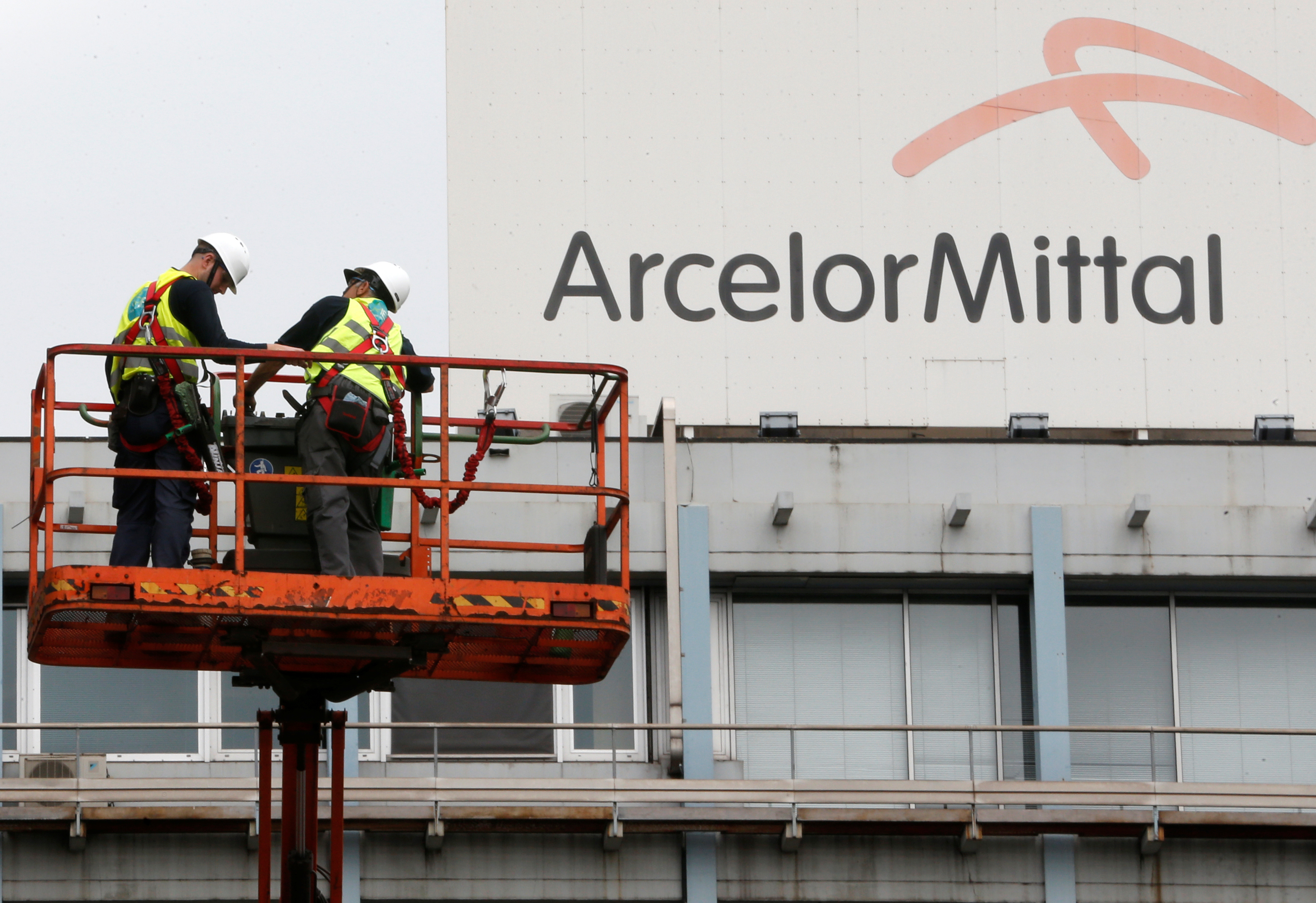 Workers stand near the logo of ArcelorMittal at the steel plant in Ghent