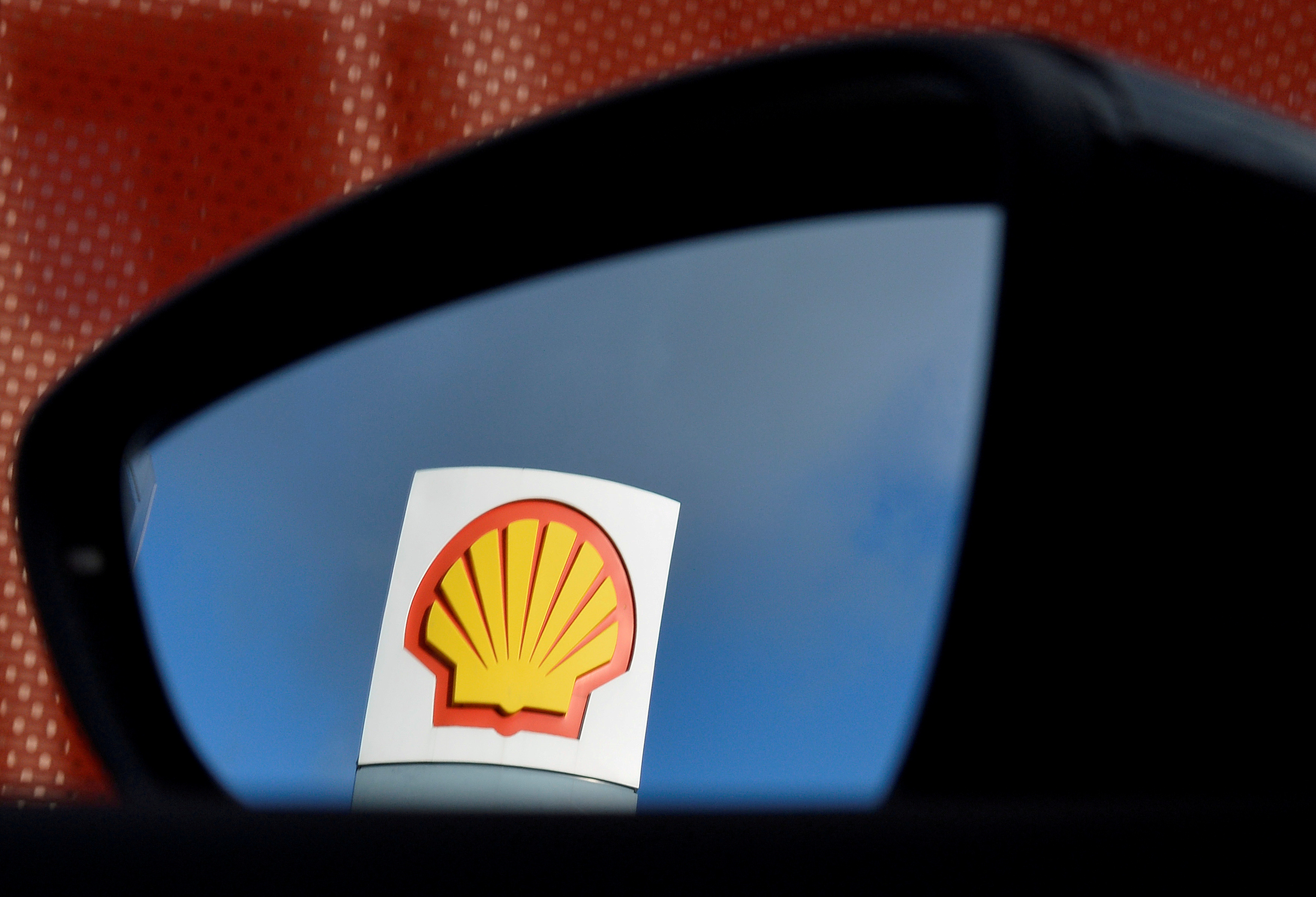 A Shell logo is seen reflected in a car's side mirror at a petrol station in west London
