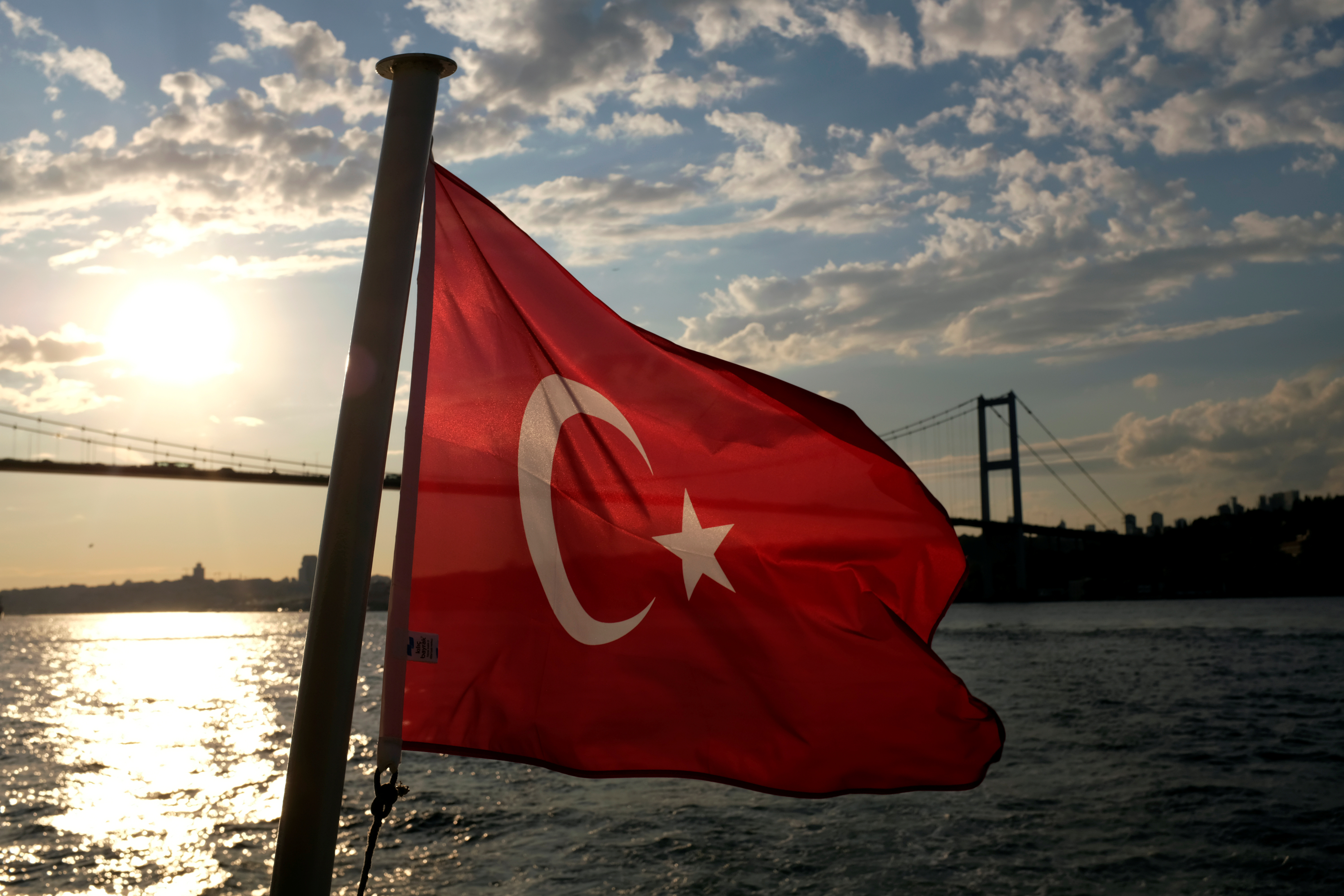 A Turkish flag with the Bosphorus Bridge in the background flies on a passenger ferry in Istanbul