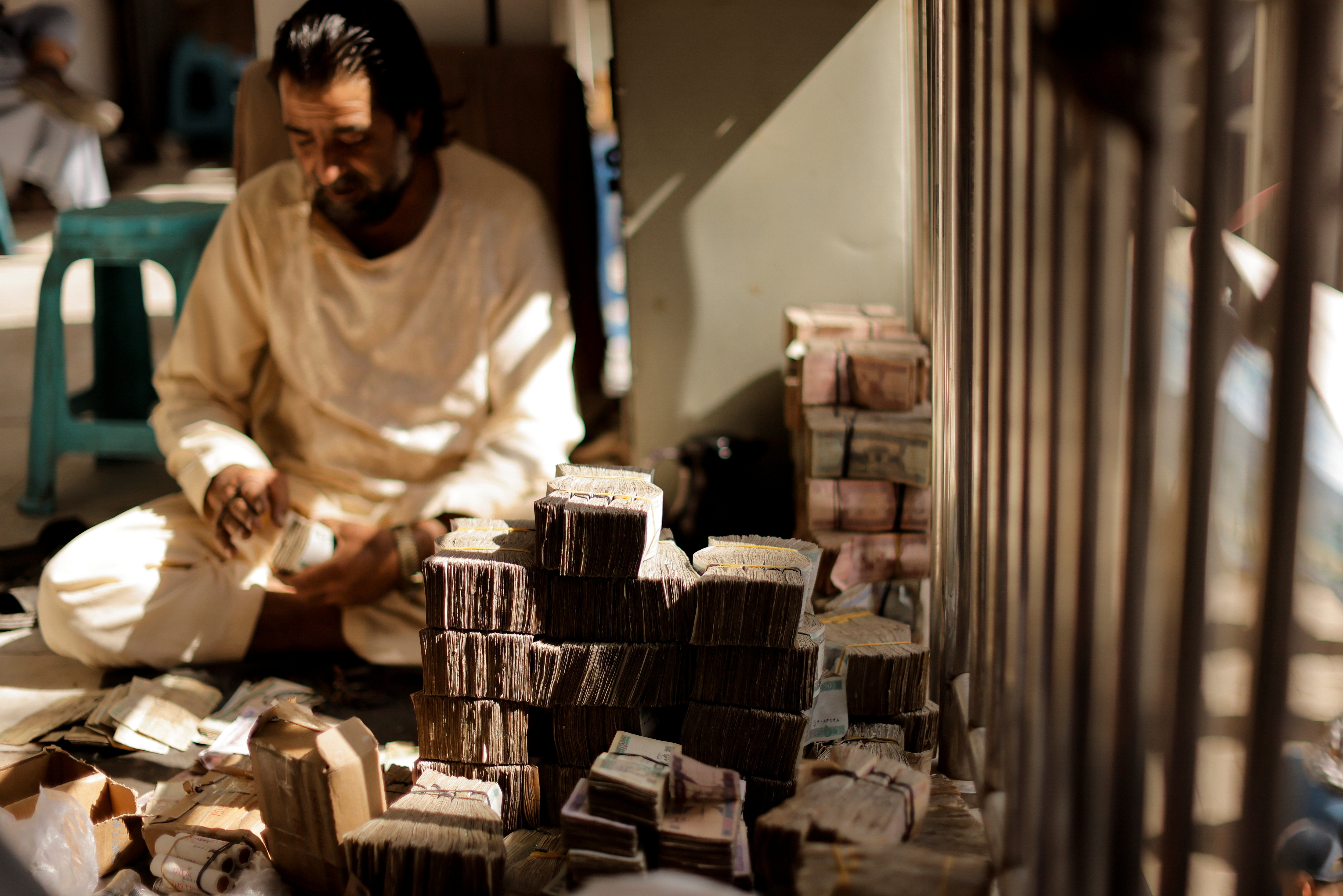 Afghan currency exchange worker stacks banknotes at a market in Kabul