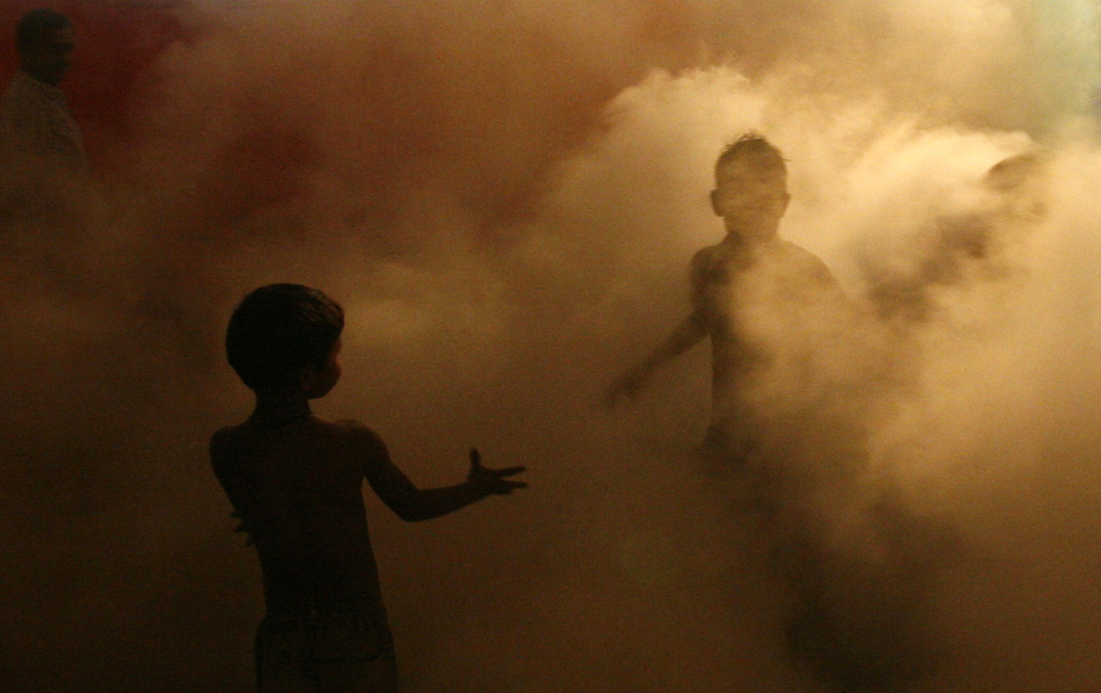 Children of local residents play through an area being fumigated by municipal workers at Noida, in the northern Indian state of Uttar Pradesh