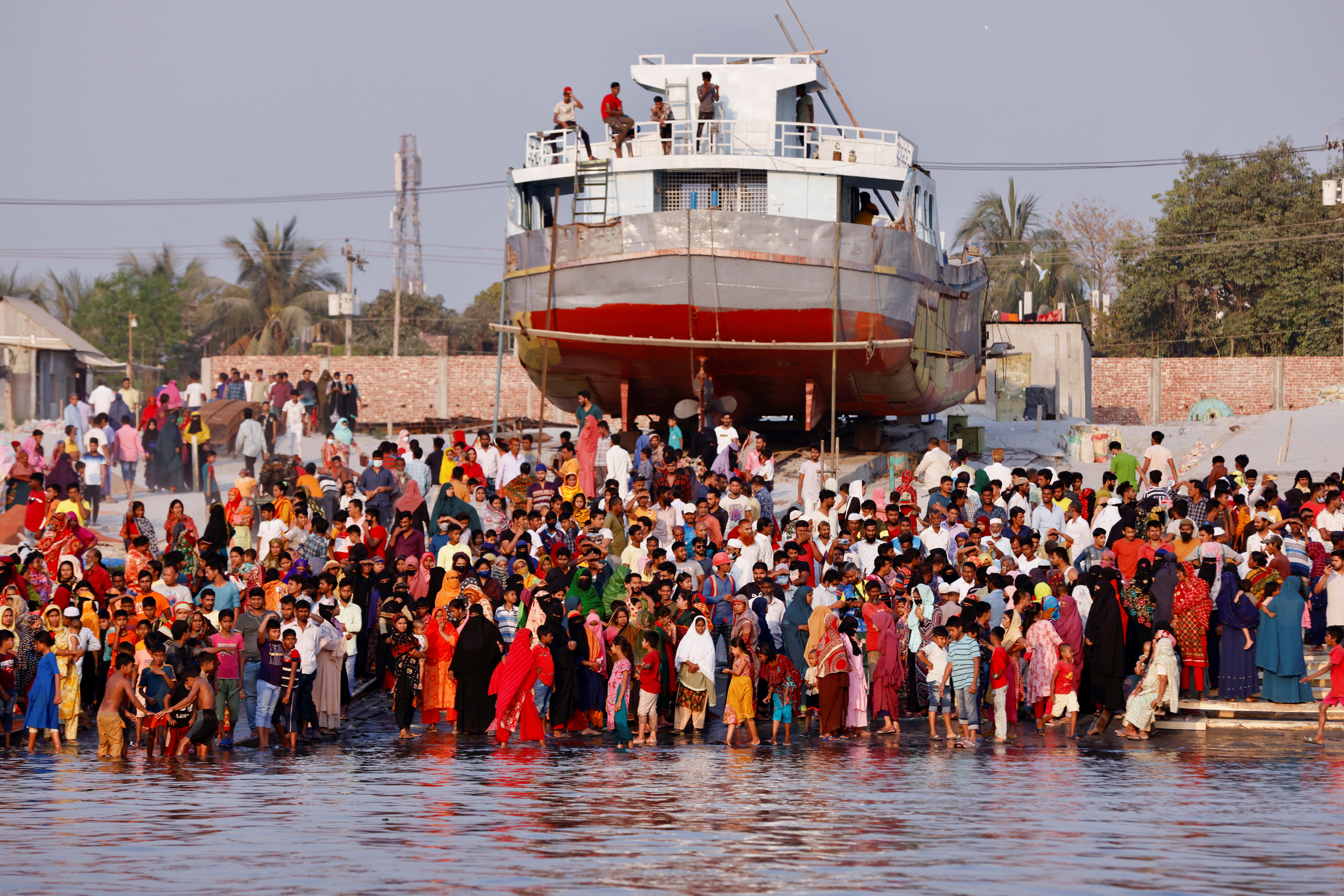 People gather at the bank of Shitalakshya river, where a ferry has sunk after colliding with a sand carrier ship in Narayanganj