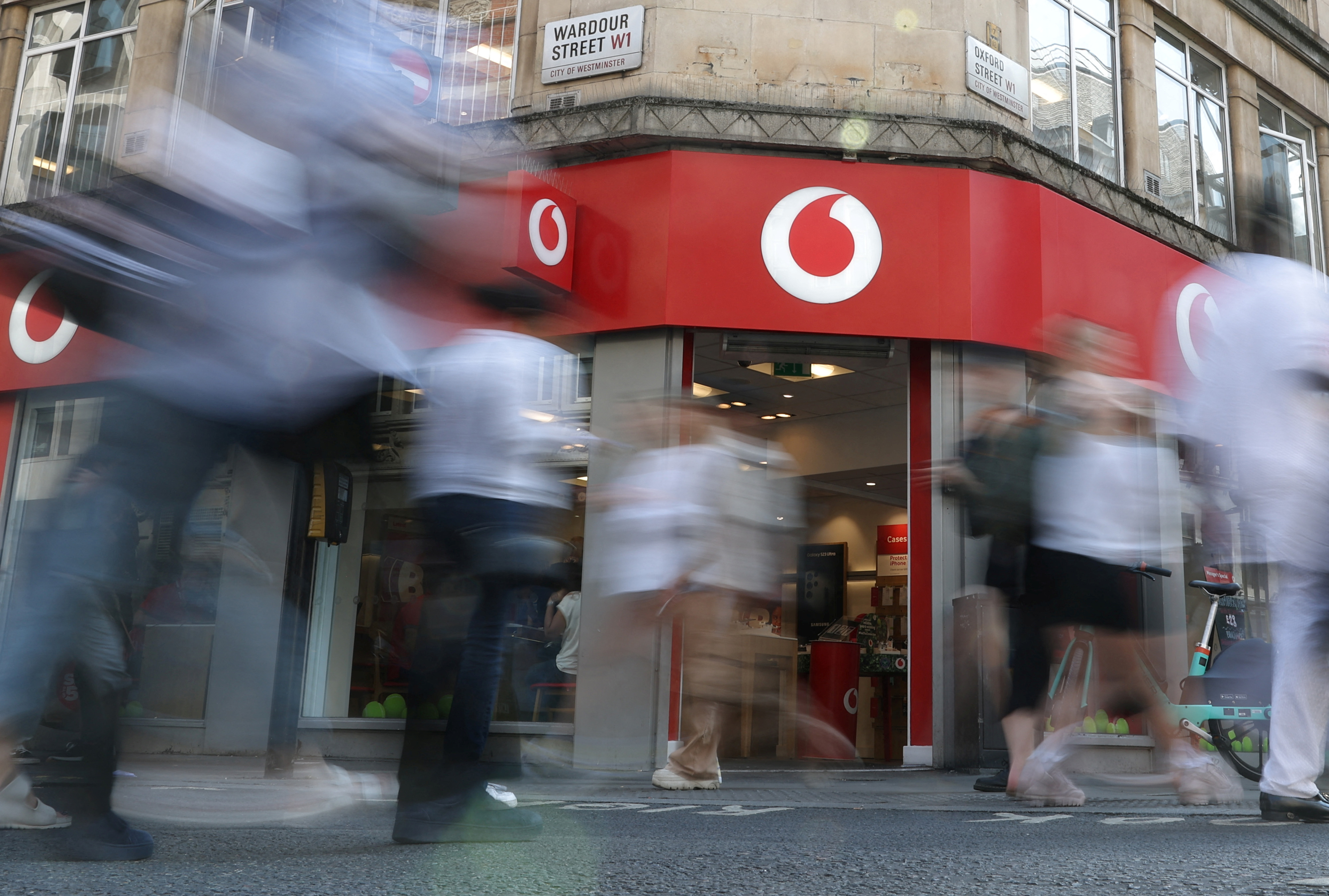 Shoppers walk past a Vodafone store in London