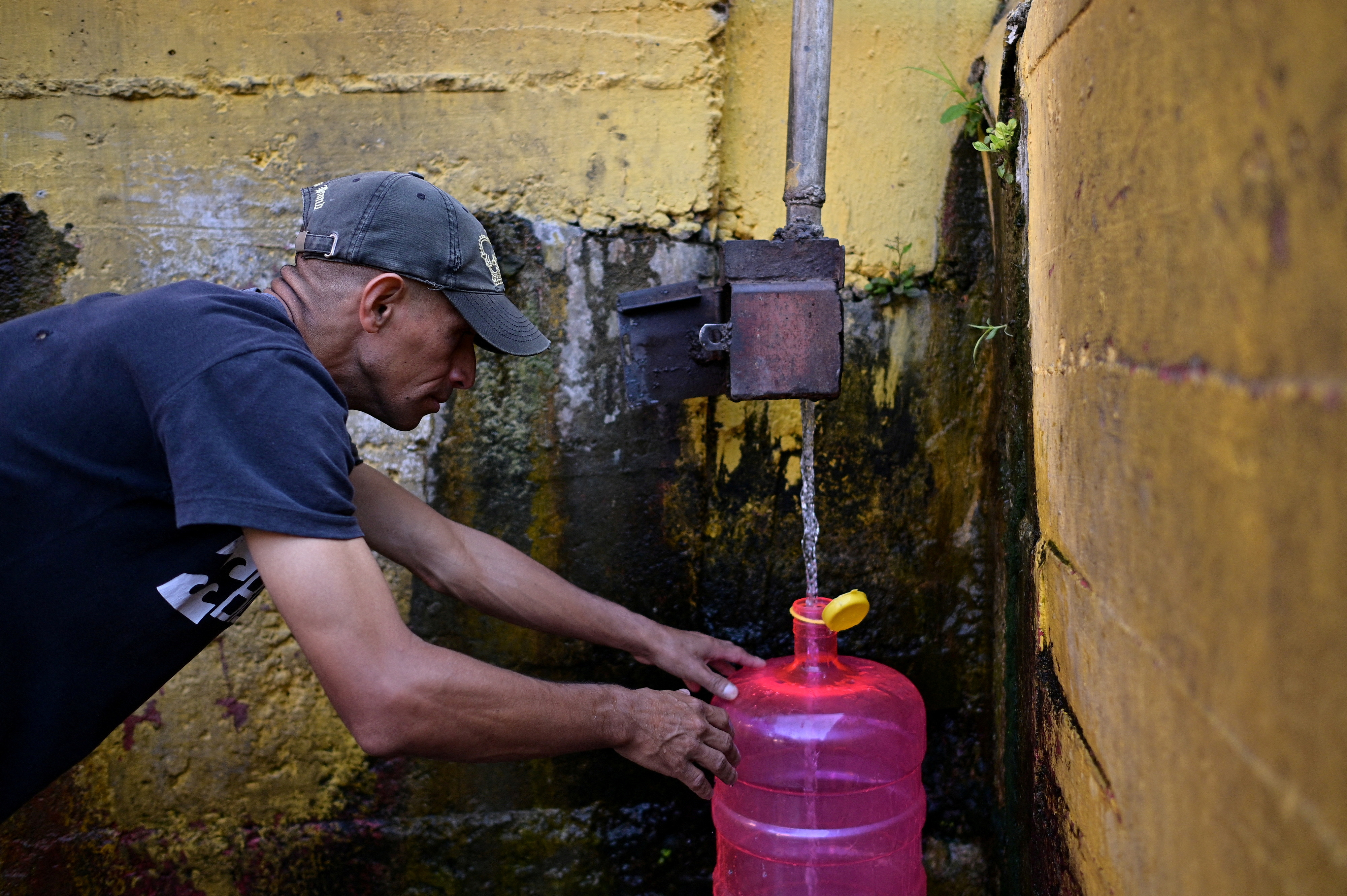 People fill plastic containers with water from a natural creek in Caracas