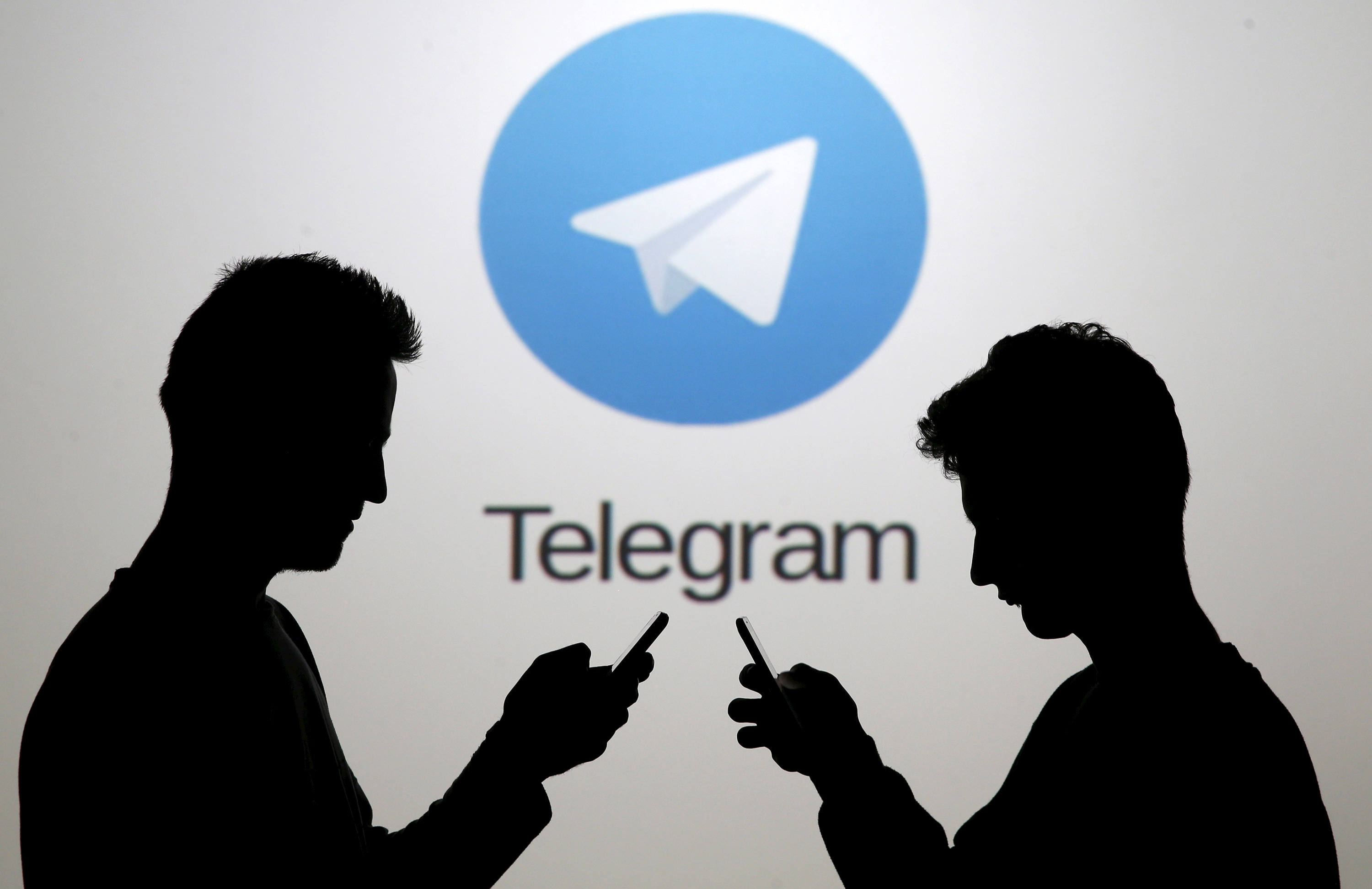 Two men pose with smartphones in front of a screen showing the Telegram logo in this picture illustration taken in Zenica