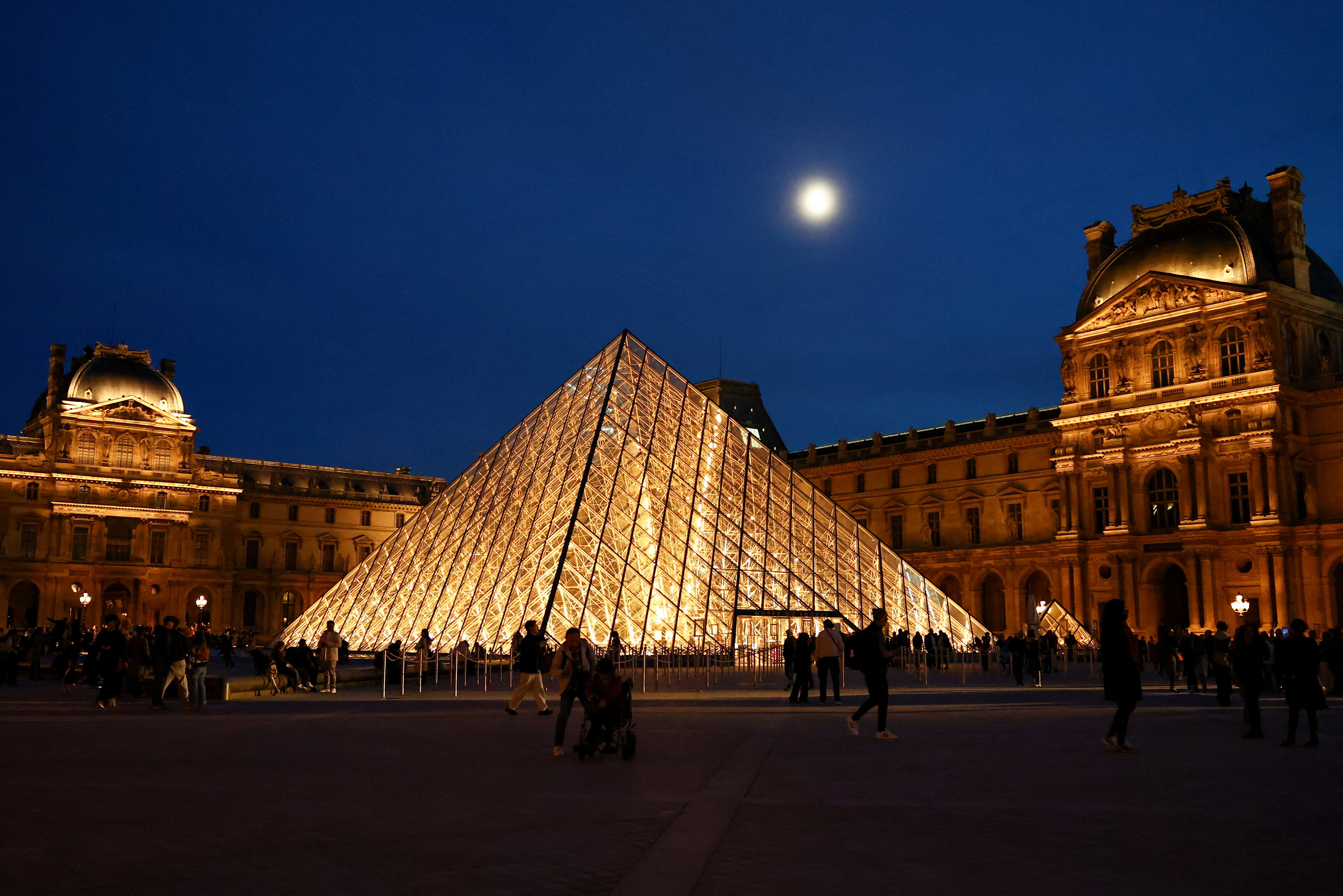 People walk near the glass Pyramid of the Louvre museum 