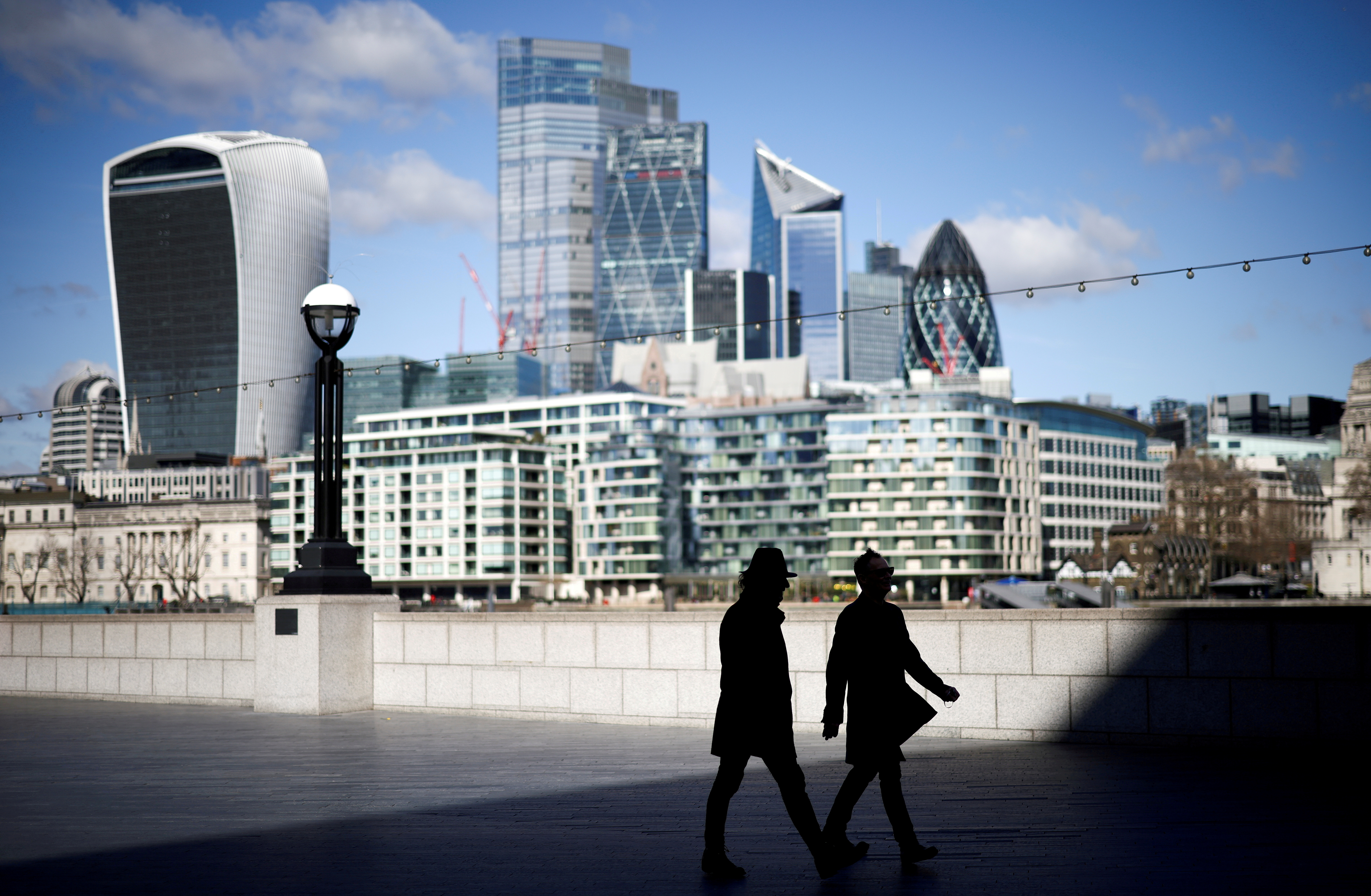 The City of London financial district can be seen as people walk along the south side of the River Thames