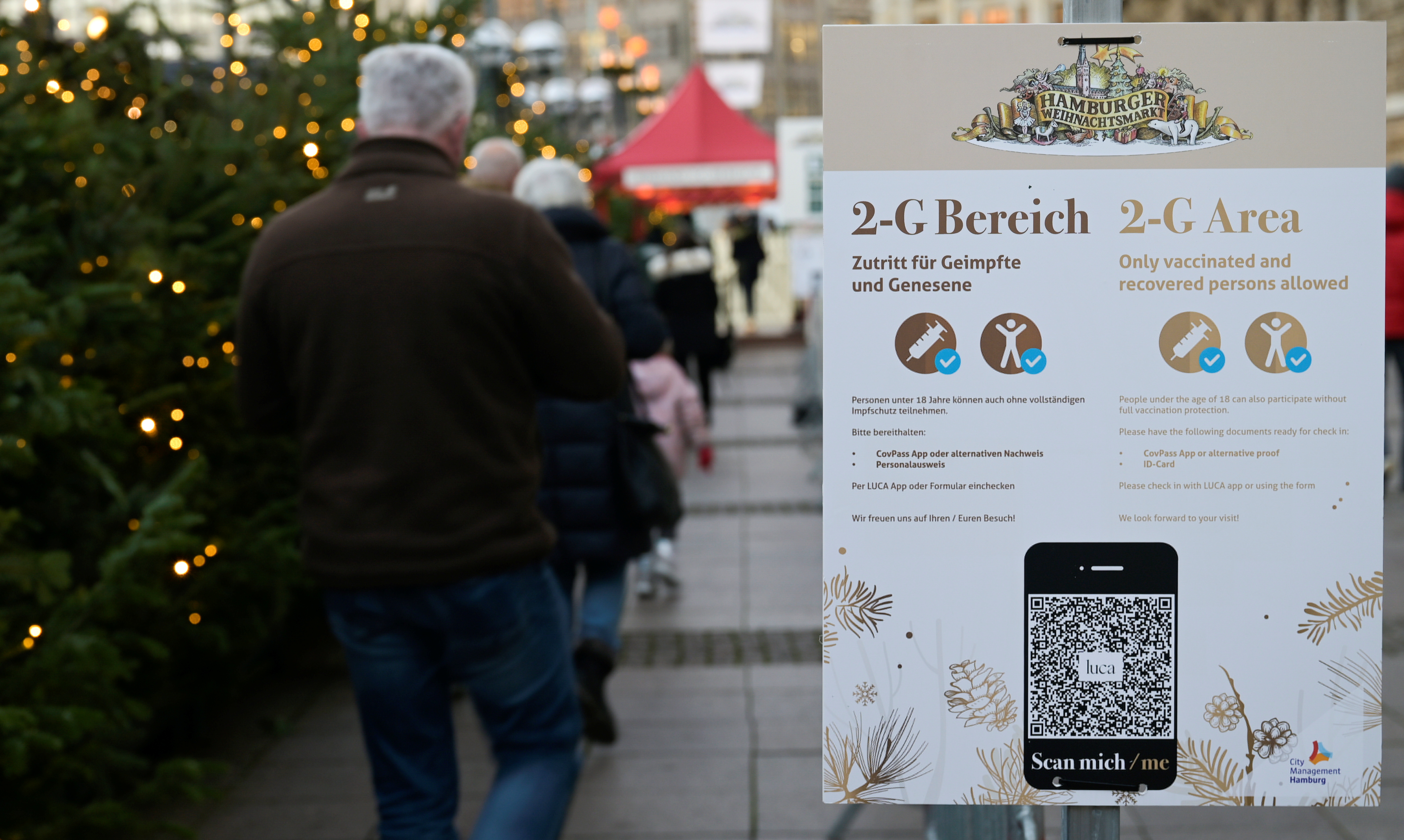 People wait in front of '2G' rule signs, allowing only those vaccinated or recovered from the coronavirus disease (COVID-19) to enter, at the entrance of the Christmas market in Hamburg, Germany November 22, 2021. REUTERS/Fabian Bimmer
