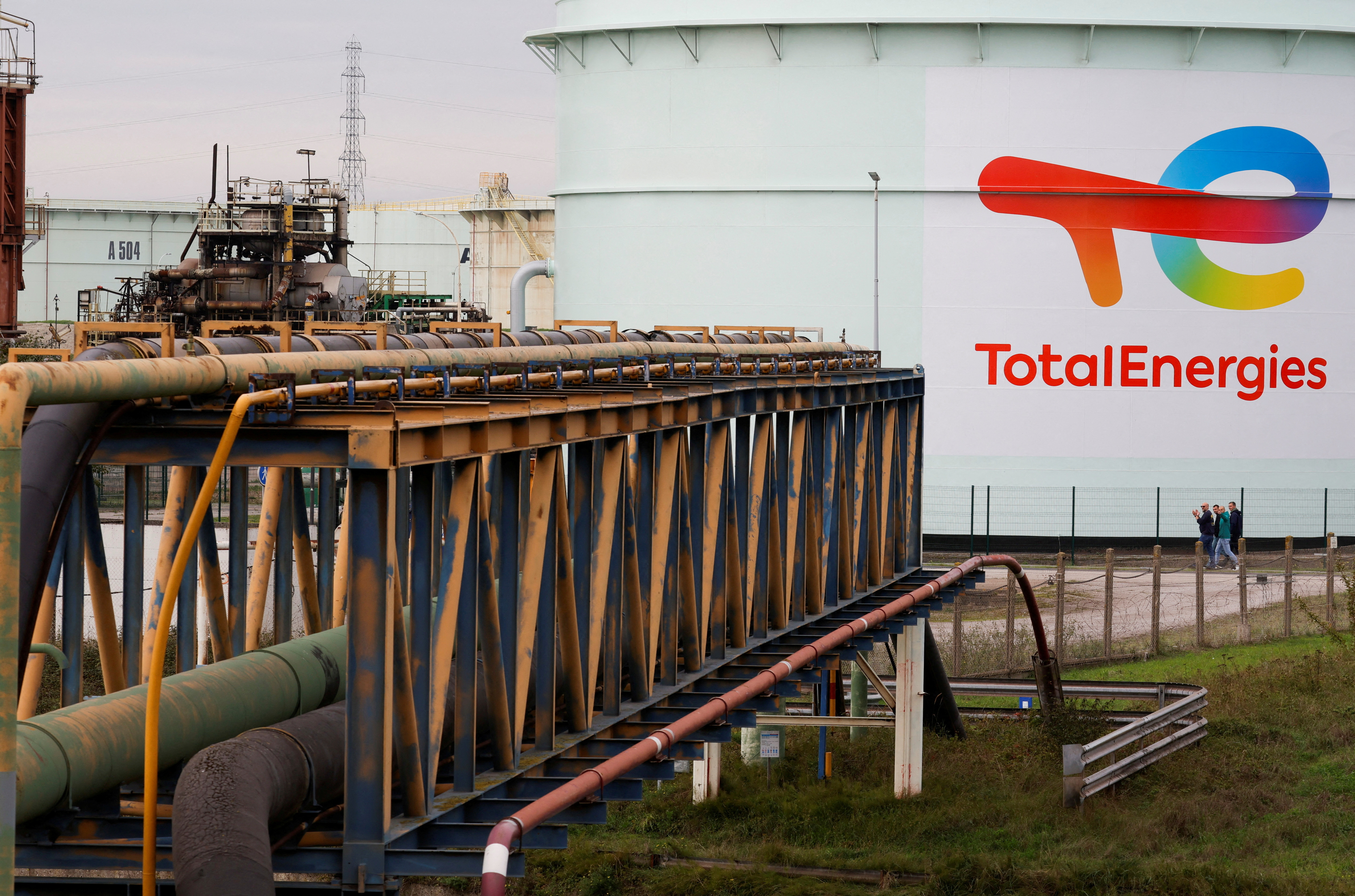 Workers of French oil giant TotalEnergies walk past an gasoline tank of the former oil refinery in Mardyck near Dunkerque