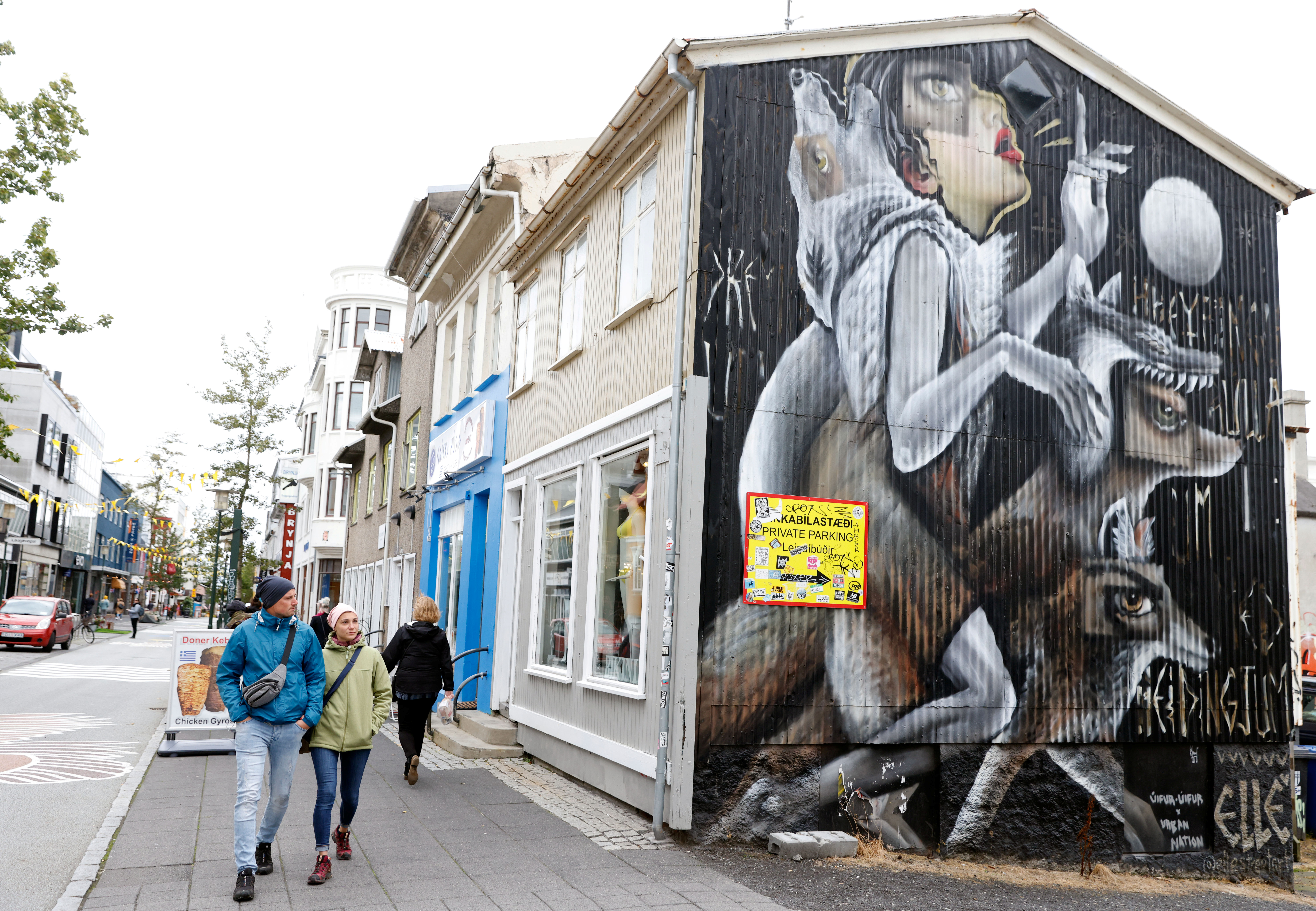 People walk past artwork on the side of a shop as the outbreak of the coronavirus disease (COVID-19) continues in Reykjavik