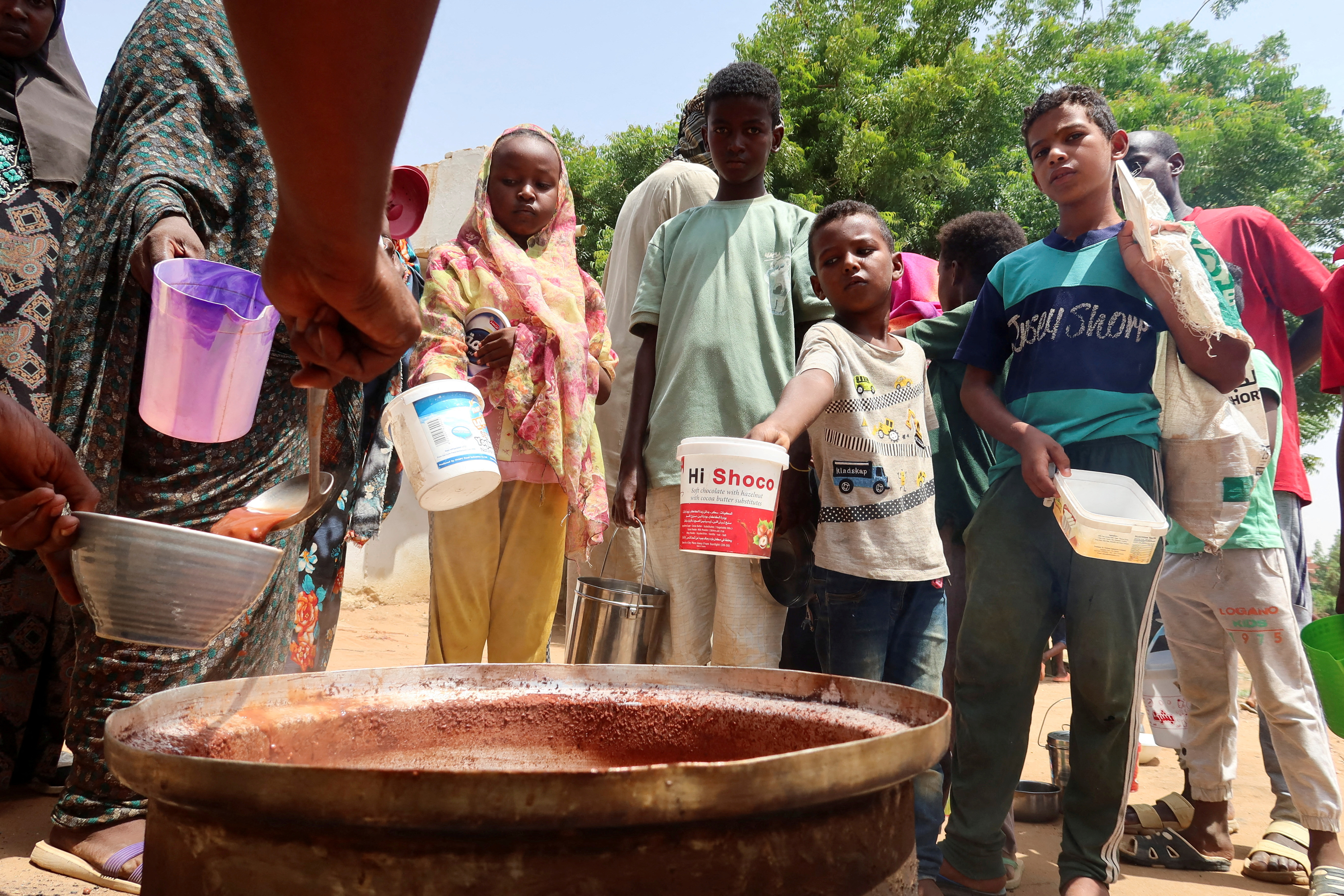 People hold pots as volunteers distribute food in Omdurman