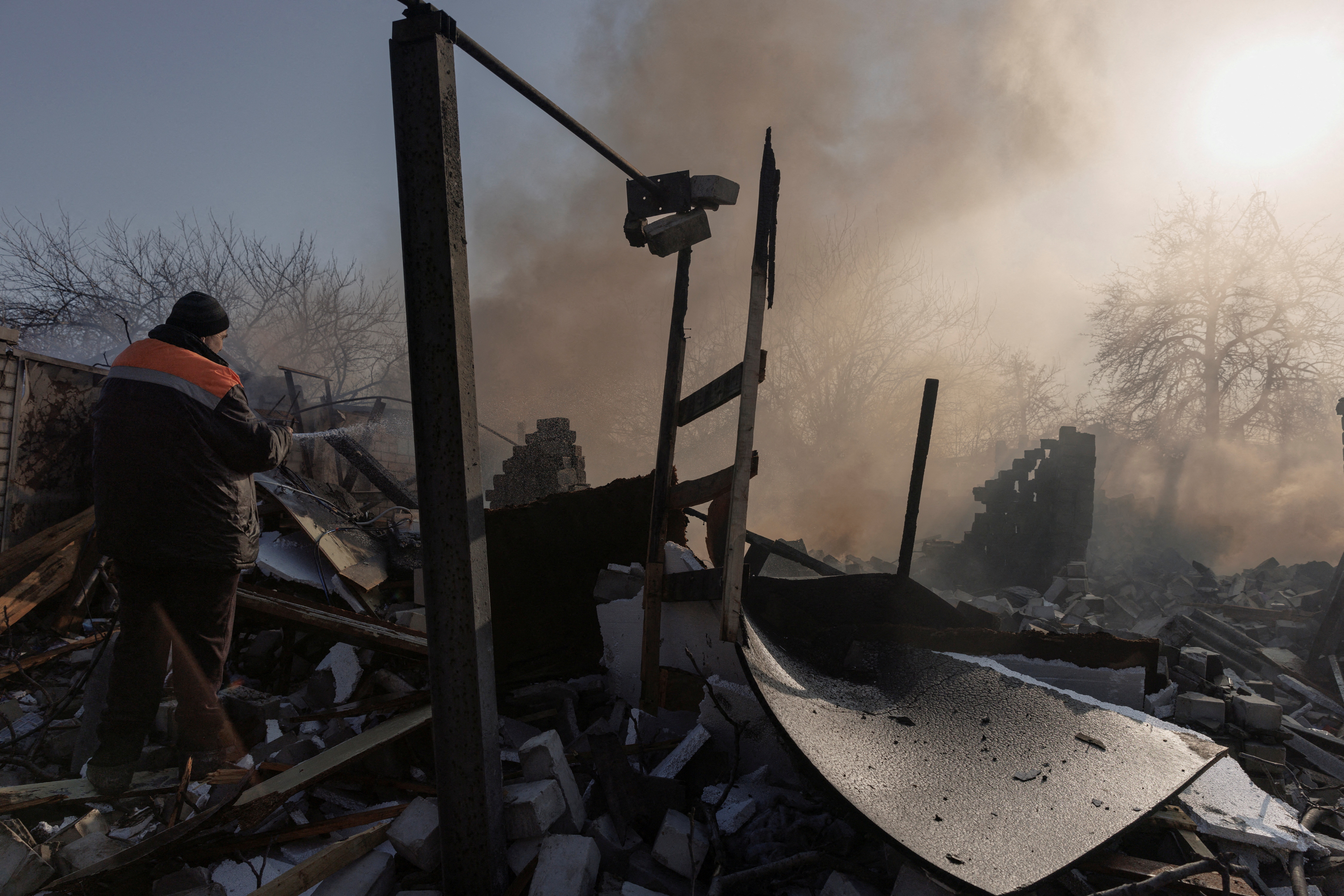A resident extinguishes a fire after a bombing destroyed a family home in a northern district of Kharkiv as Russia's attack on Ukraine continues