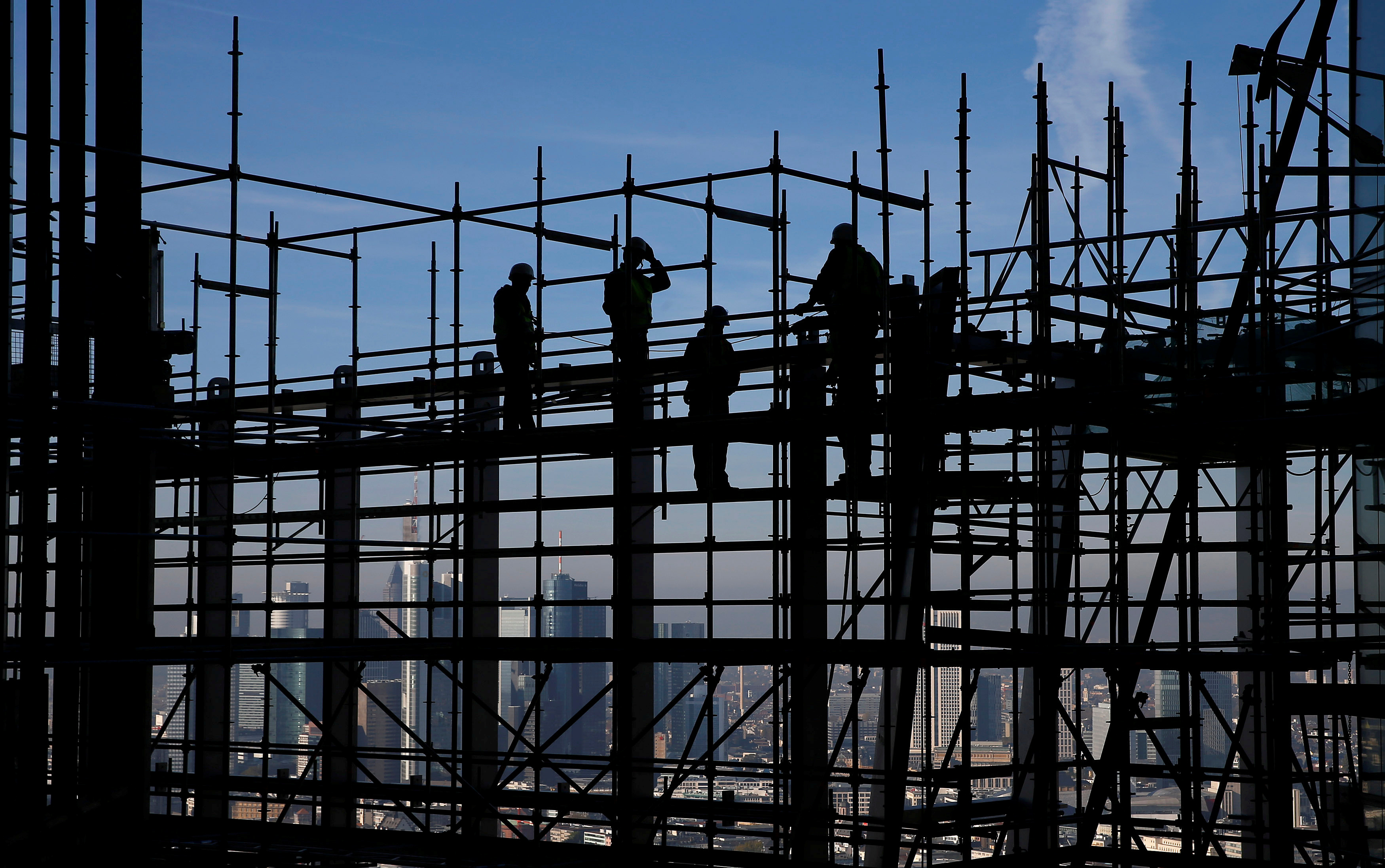 Construction workers are silhouetted while standing on scaffolding at the construction site of the new headquarters of the  ECB during a guided media tour in Frankfurt