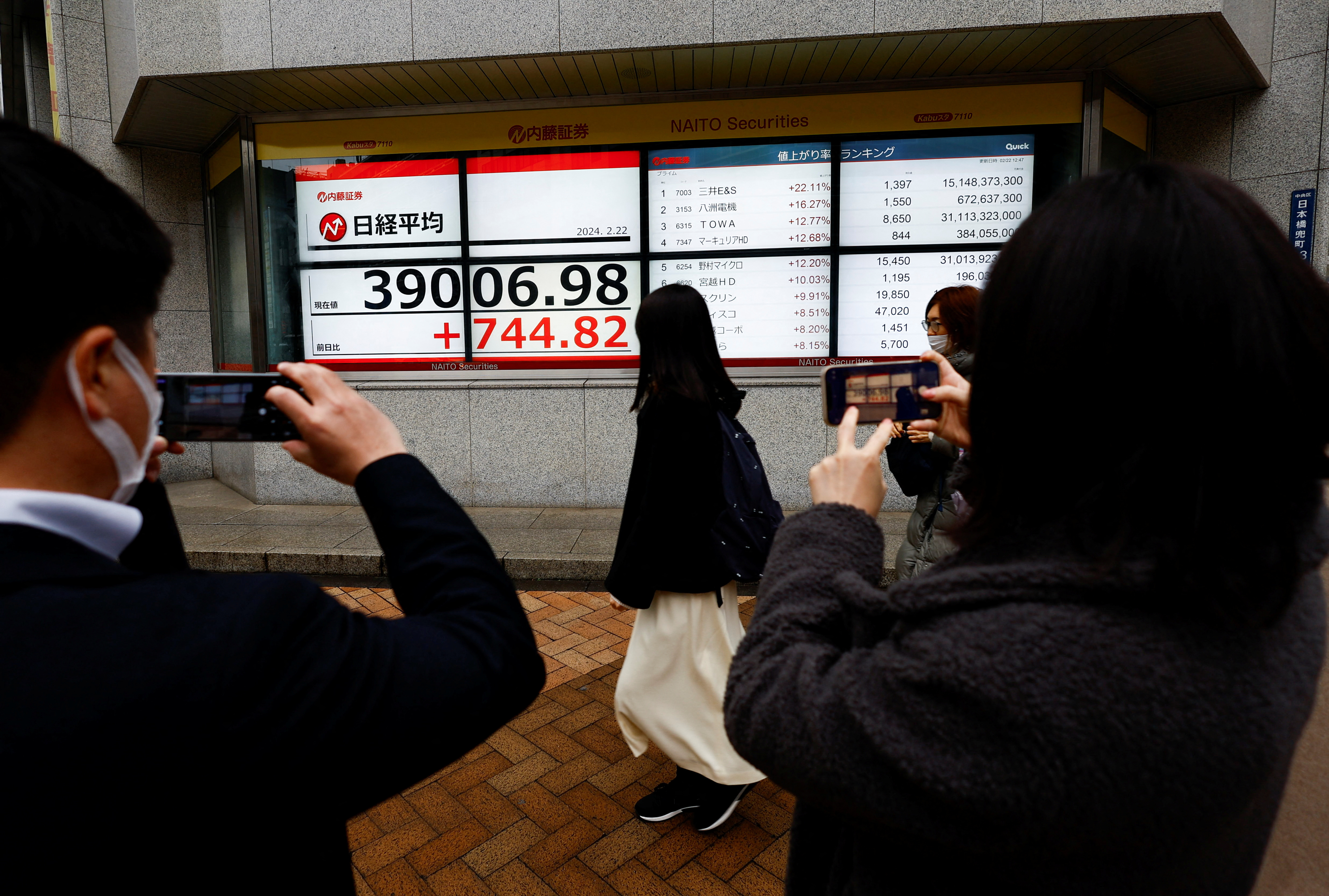 People using their smartphones take photos of  electronic screens displaying Japan's Nikkei share average surged past an all-time record high scaled in December 1989 in Tokyo