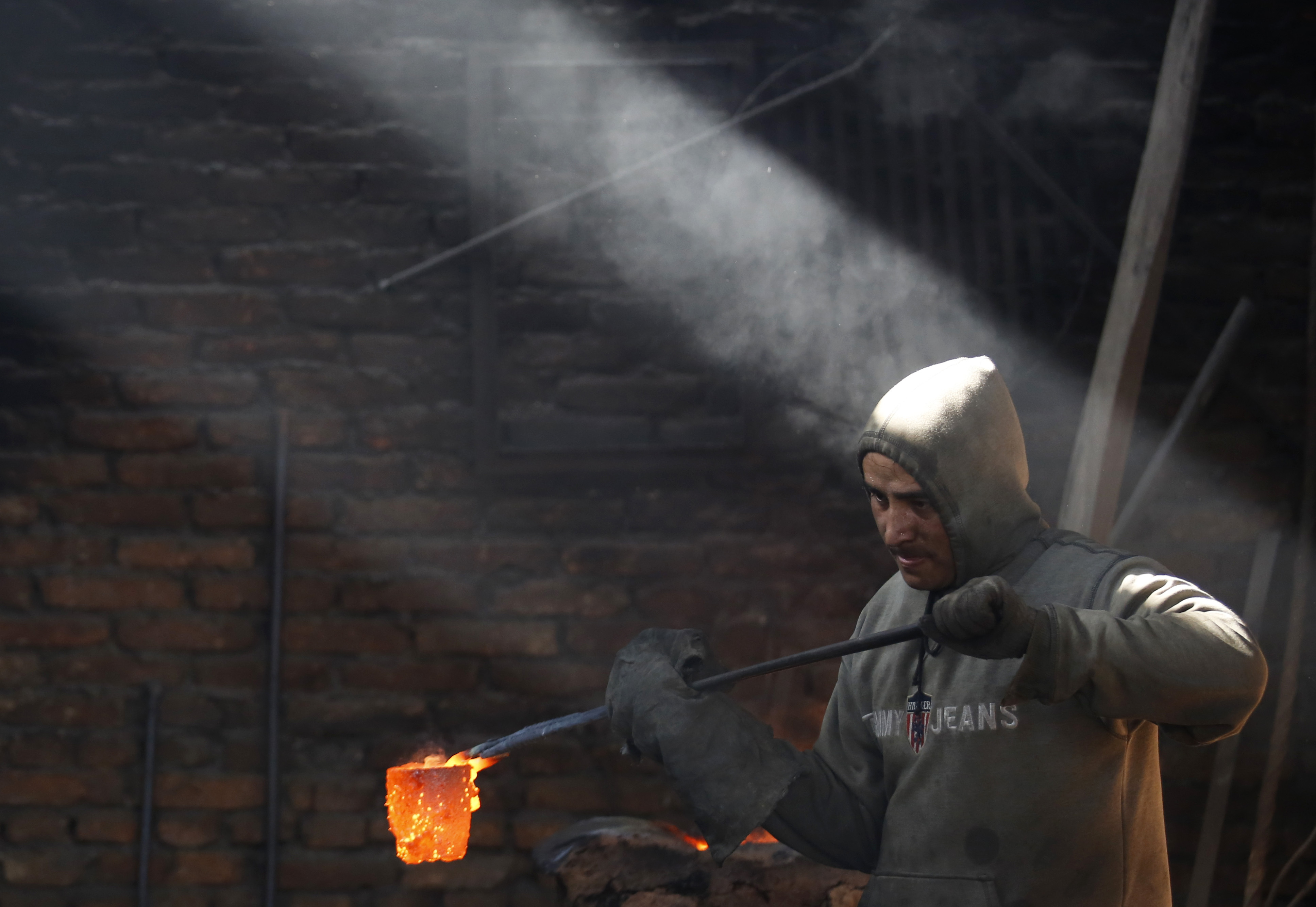 A worker carries a crucible of melted copper as he makes statues at a workshop in Lalitpur