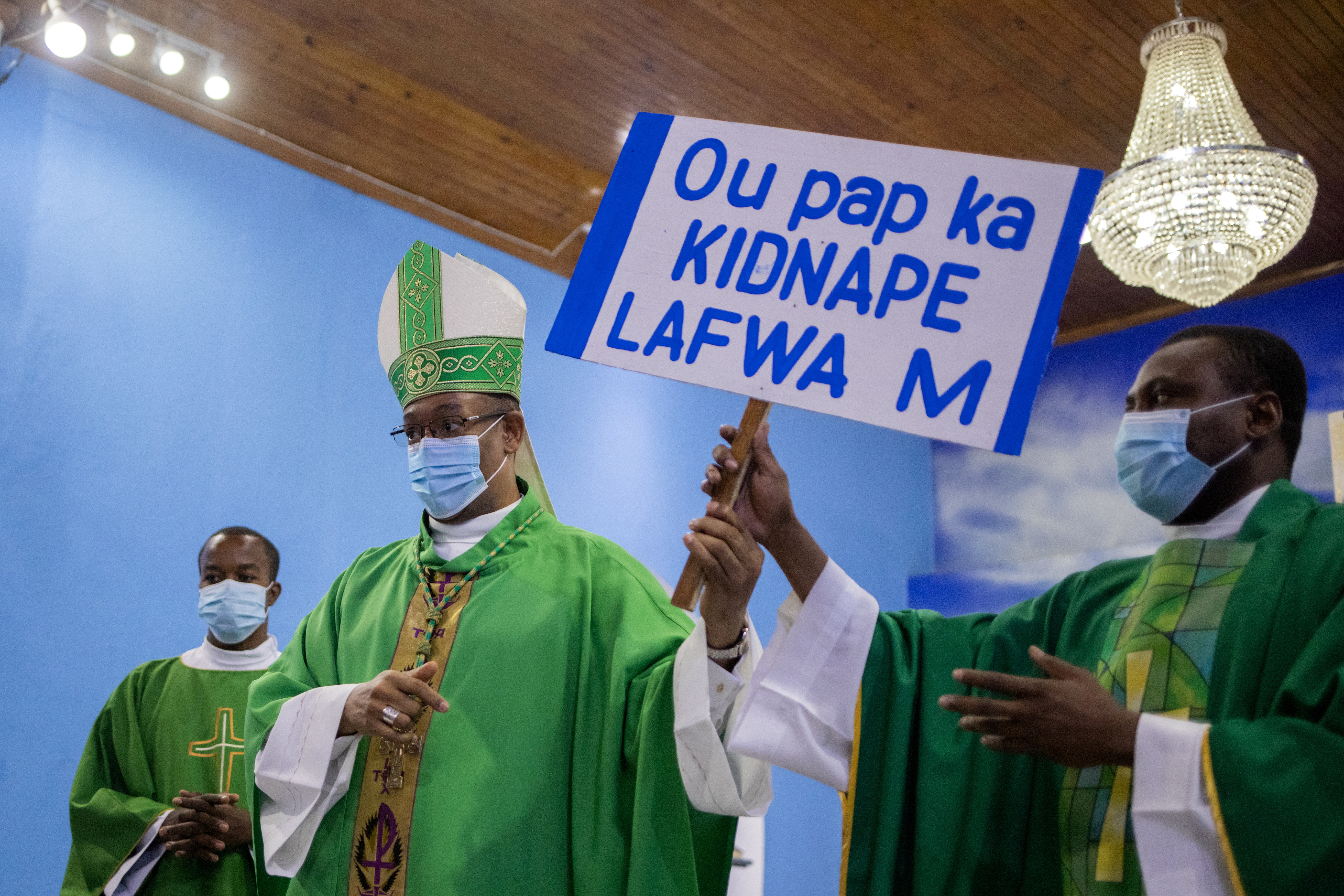Max Leroy Mesidor, the Metropolitan Archbishop of Port-au-Prince, hands off a placard that reads 