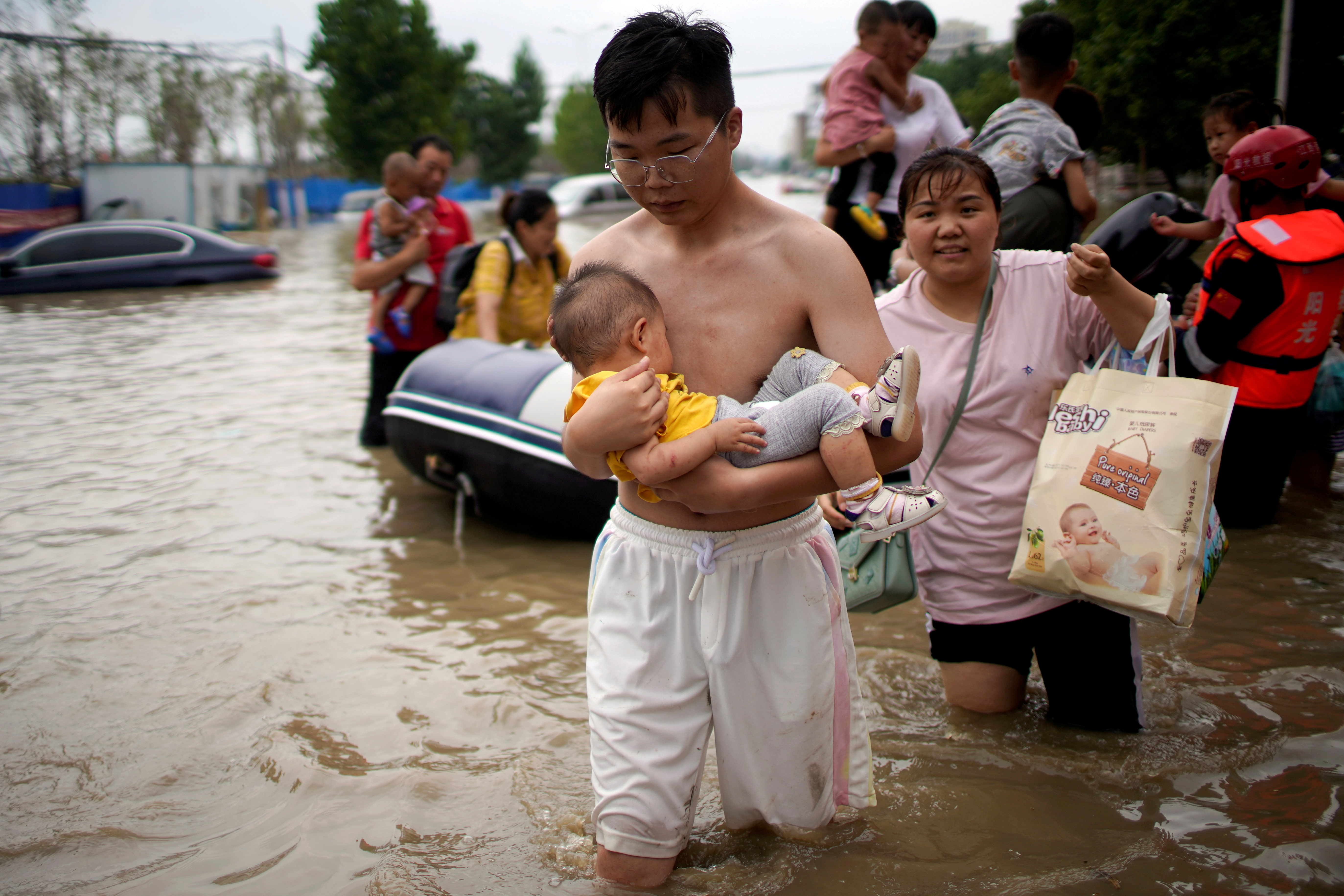 Man holding a baby wades through a flooded road following heavy rainfall in Zhengzhou