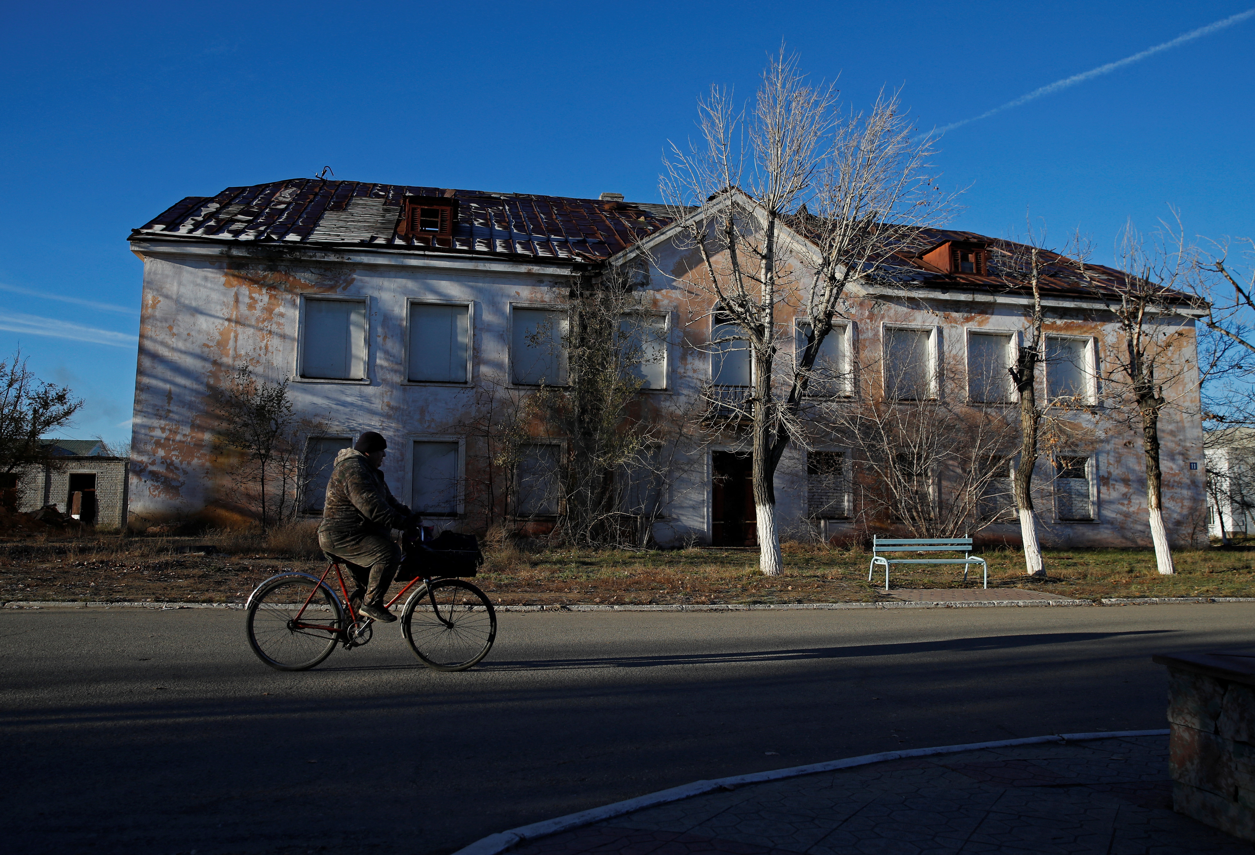 A man rides a bicycle past an abandoned building in Kurchatov