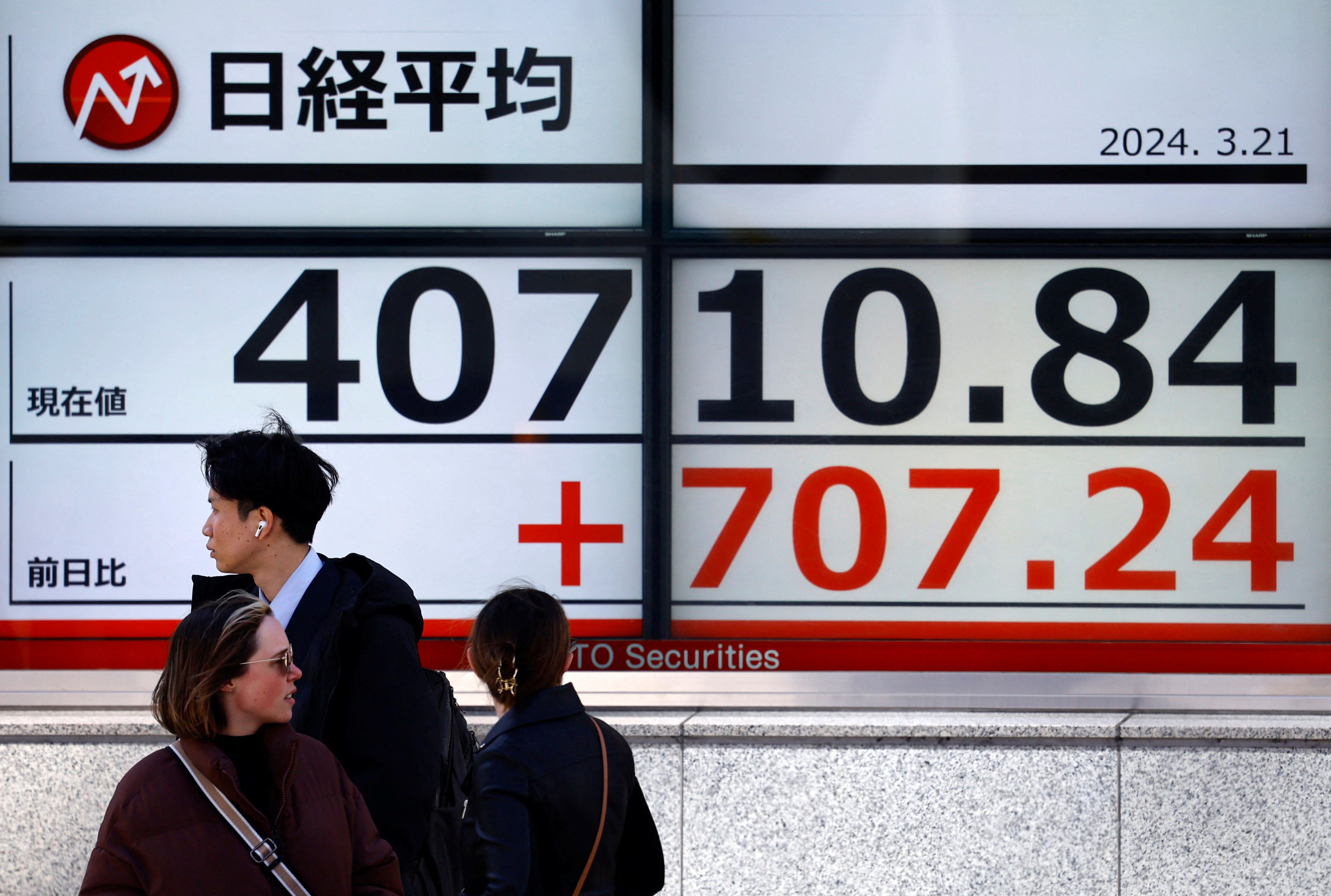 Passersby walk in front of an electric screen displaying Japan's Nikkei share average outside a brokerage in Tokyo