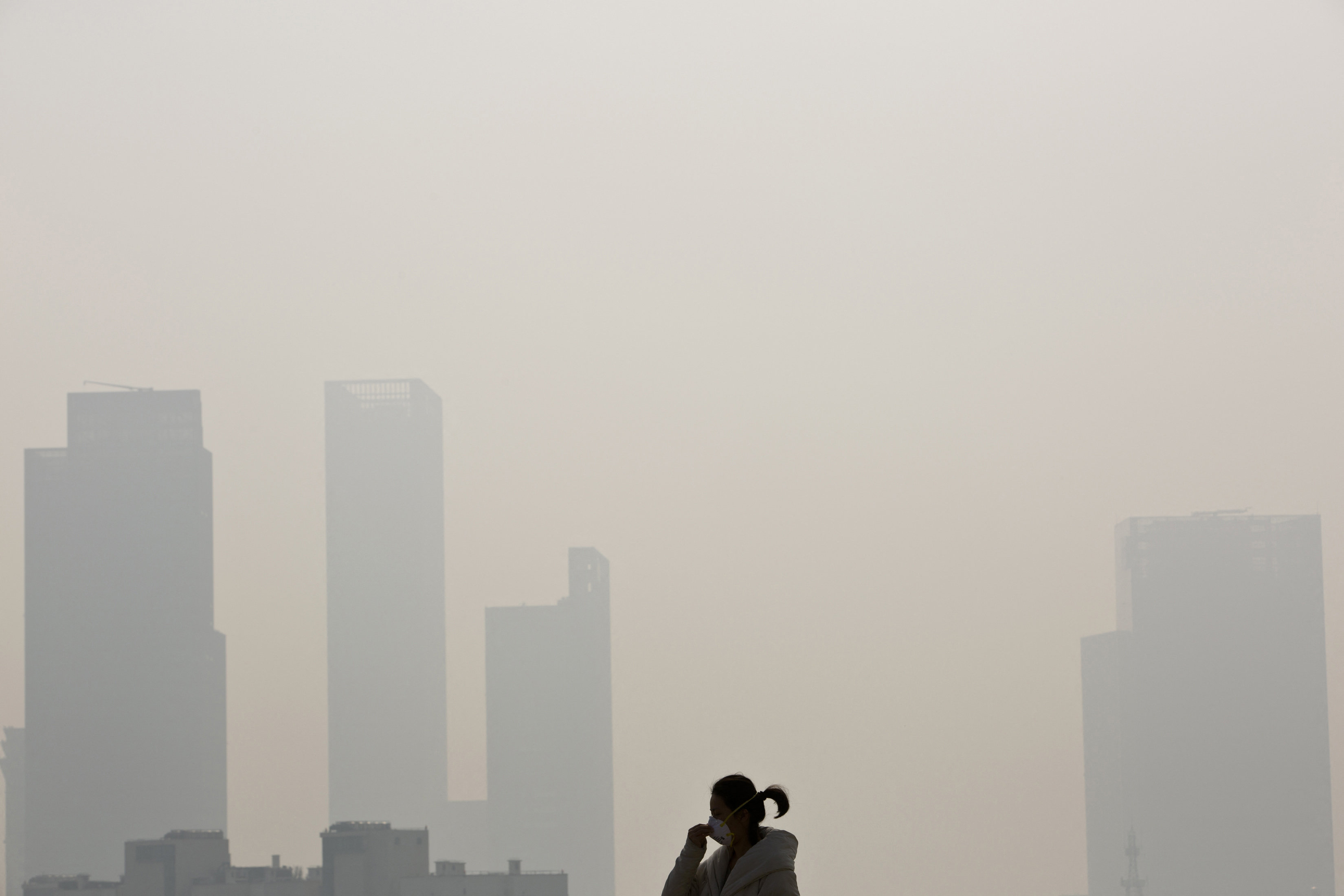 A woman wearing a mask walks on a bridge during a hazy day in downtown Shanghai December 5, 2013.  REUTERS/Aly Song  