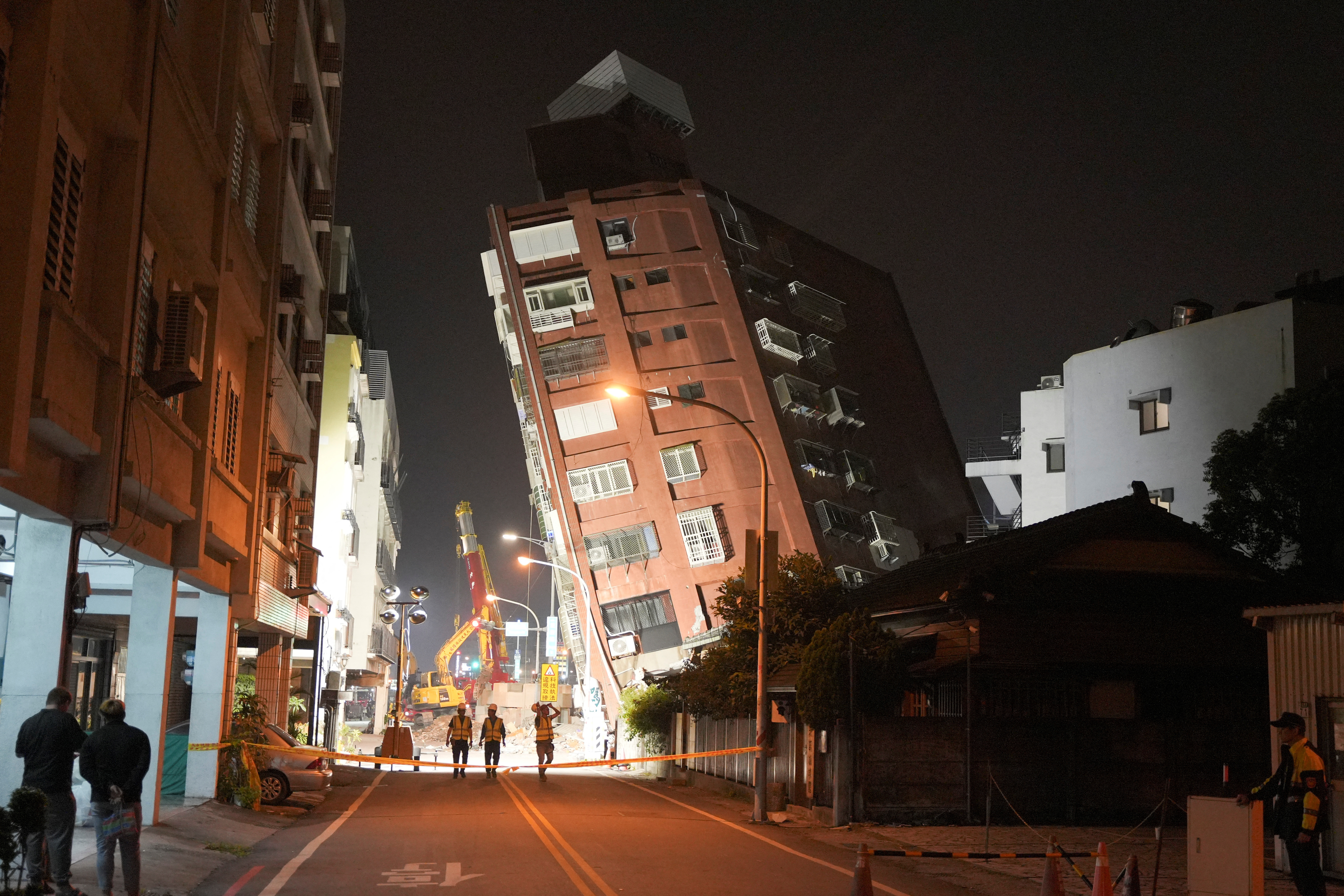 Workers walk at the site where a building collapsed following an earthquake, in Hualien