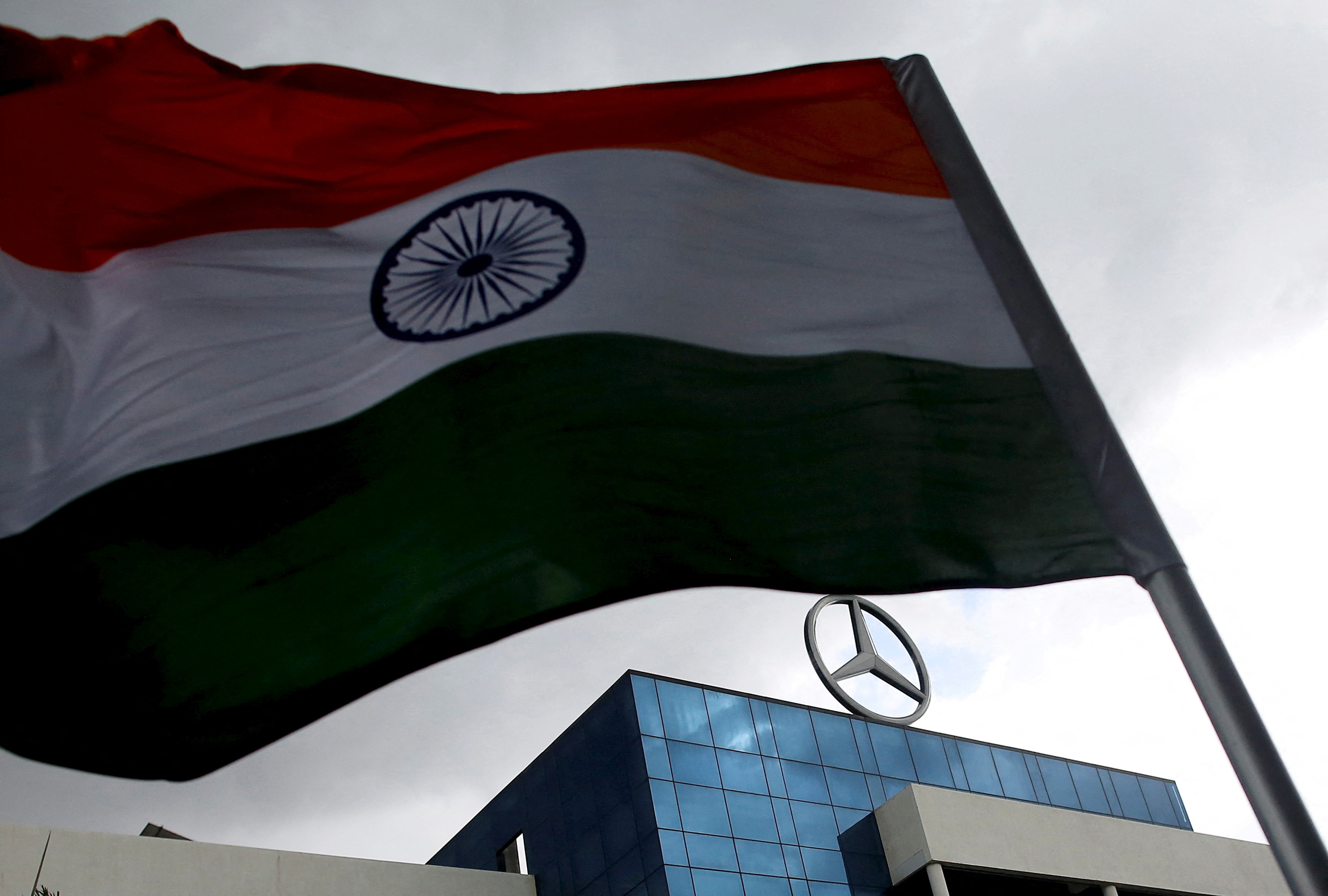 An Indian national flag is seen in front of a logo of Mercedes-Benz at the company's vehicle assembly plant in Chakan