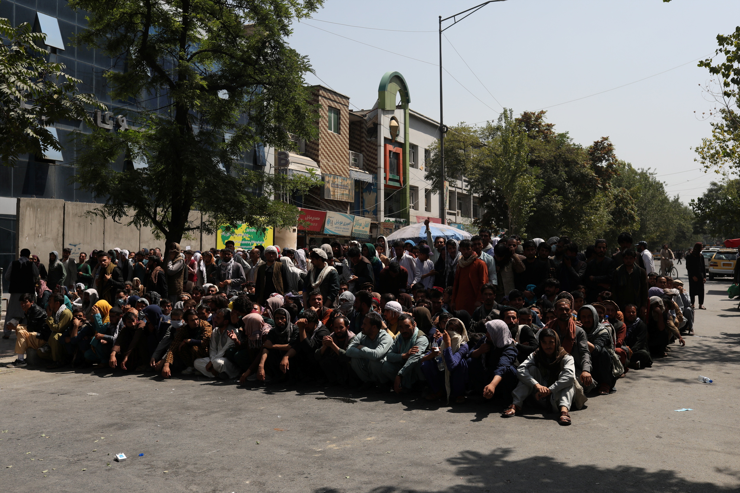 Afghans wait to visit a bank on a street in Kabul