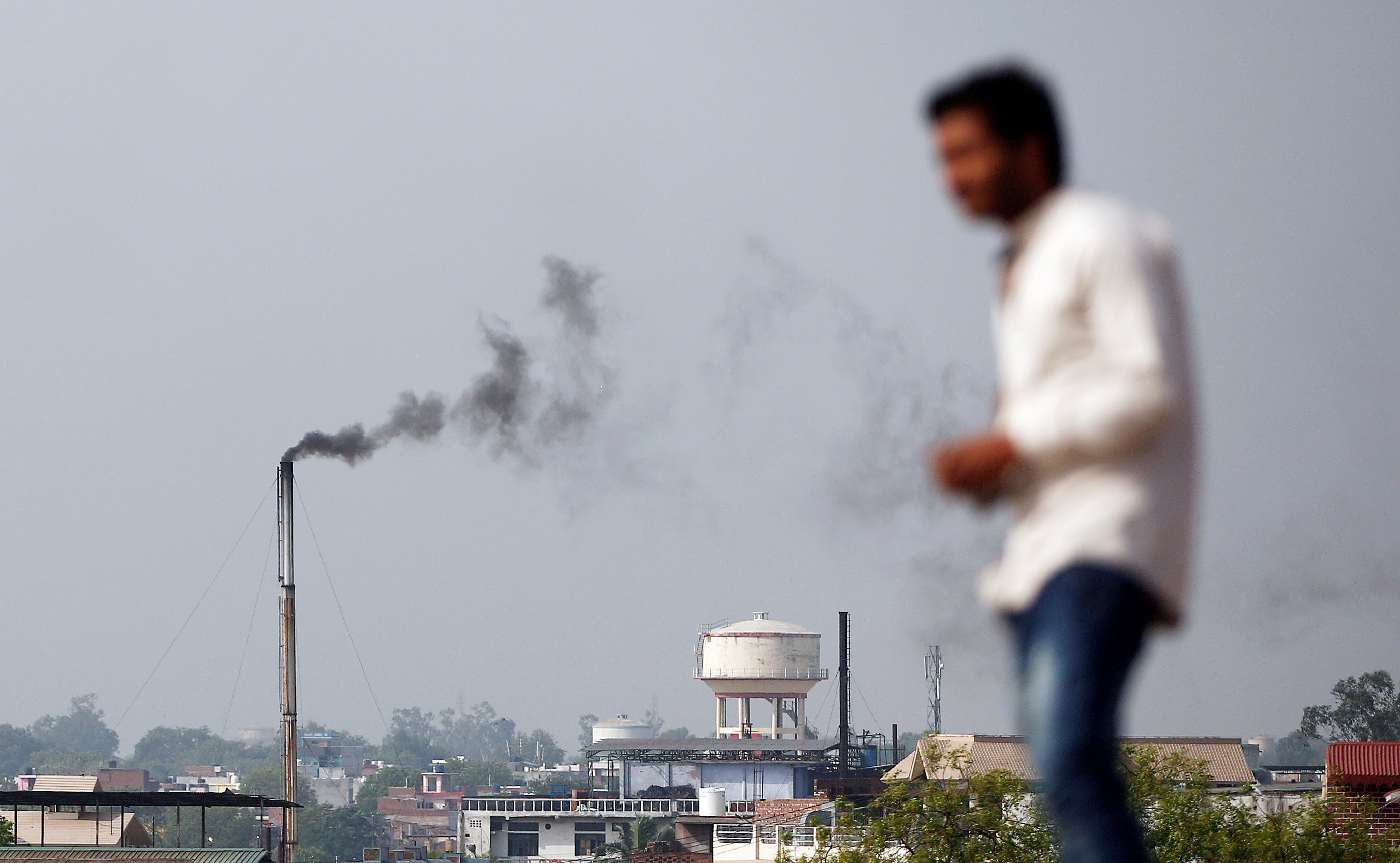 A man stands on a hill as smoke emits from a chimney of a leather tannery at an industrial area in Kanpur