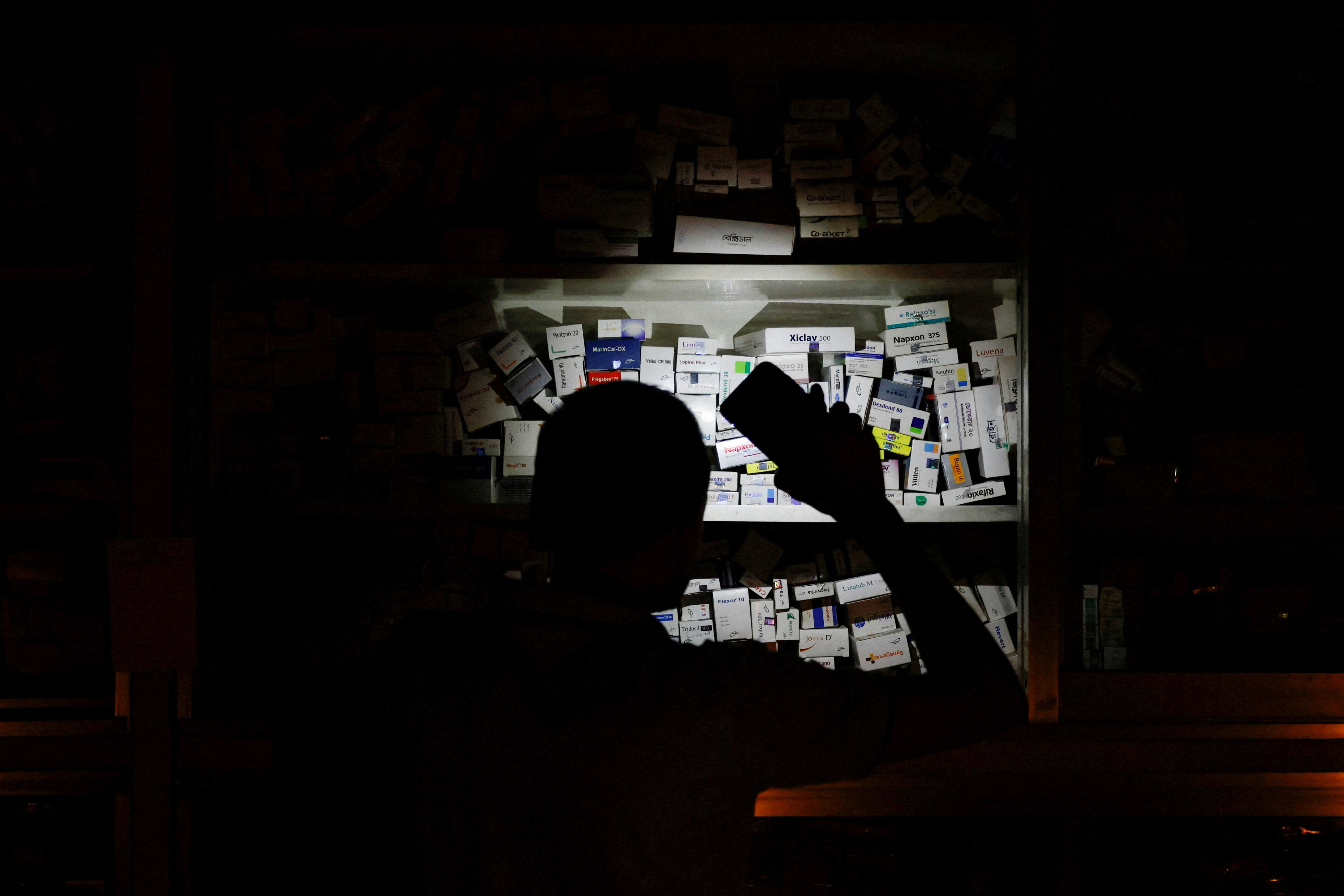 A salesman of a pharmaceutical shop uses his cellphone torch to find medicine to serve customers during countrywide blackout in Dhaka