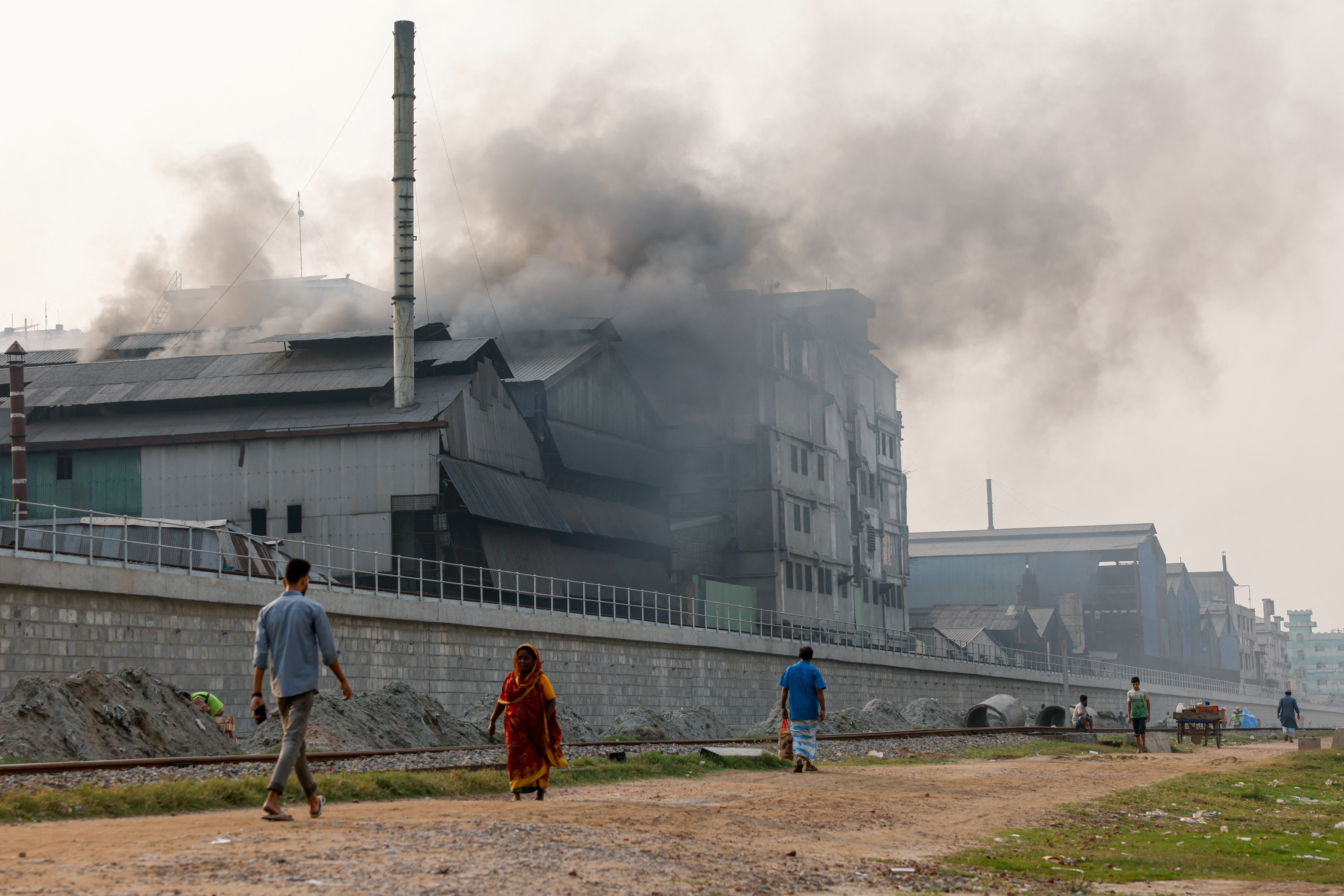 Commuters pass an industrial area as smoke rises from re-rolling factories at the Shyampur area of Dhaka