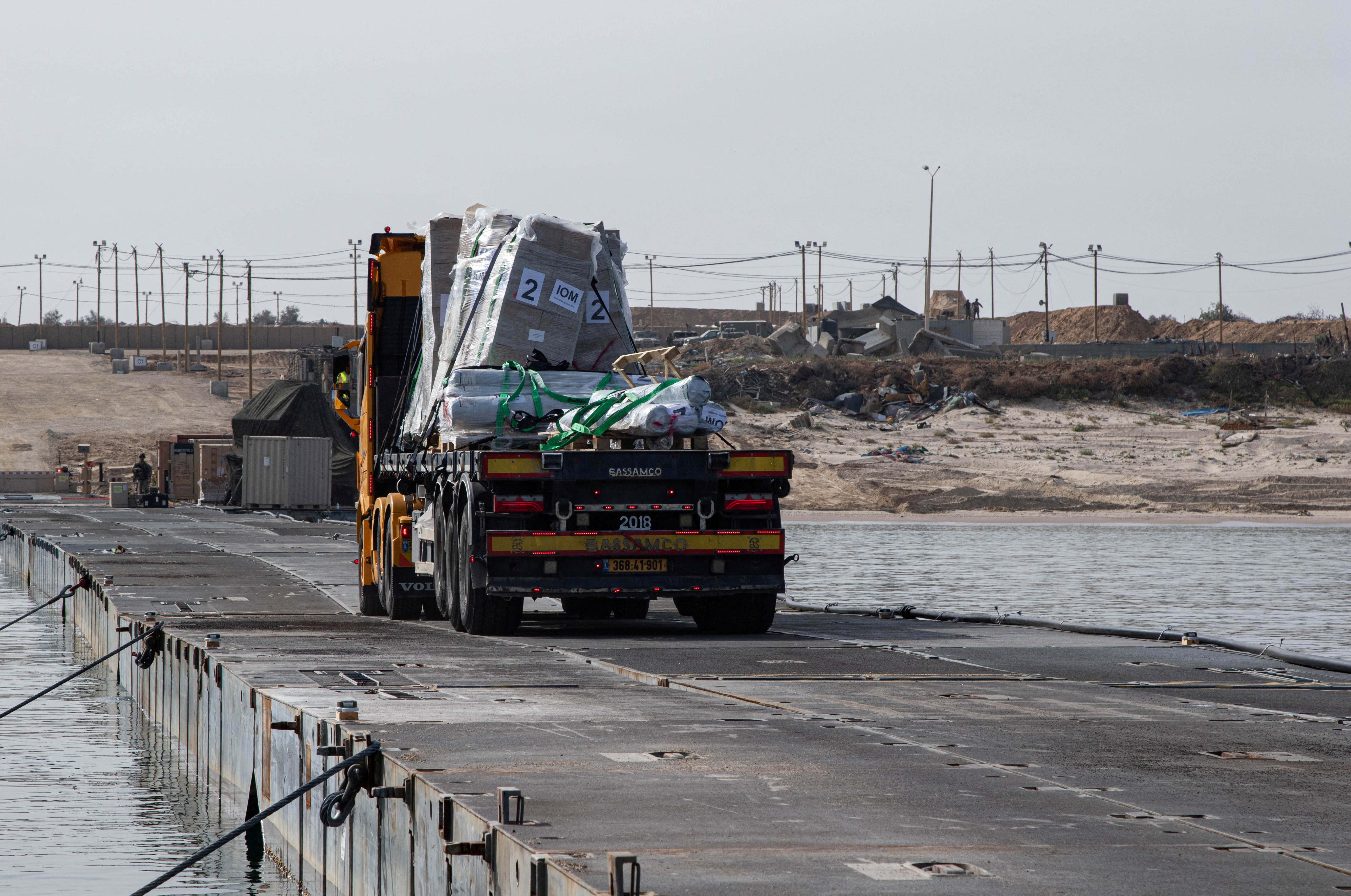 Trucks deliver humanitarian aid over a temporary pier on the Gaza coast