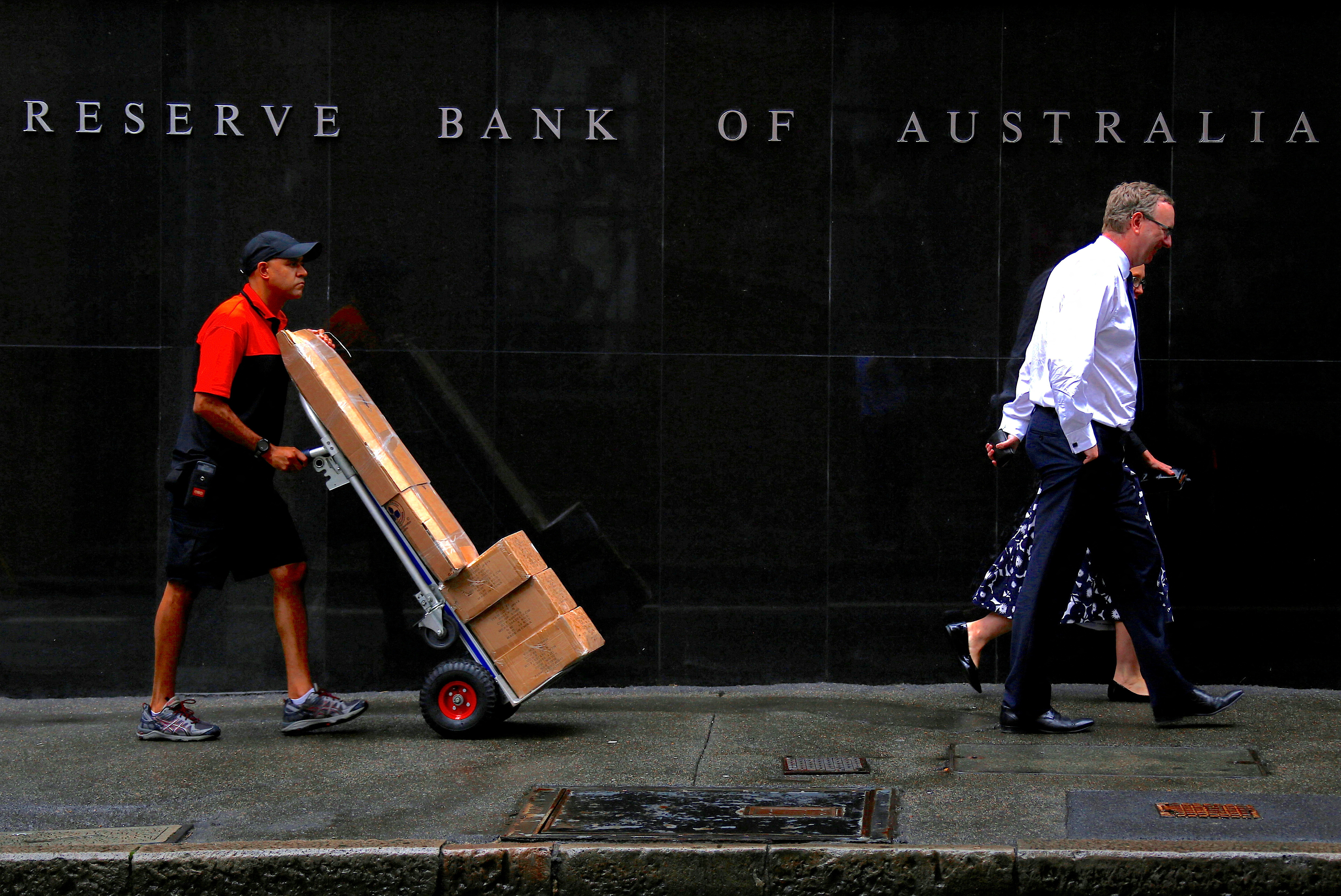 A worker pushing a trolley walks with pedestrians past the Reserve Bank of Australia (RBA) head office in central Sydney