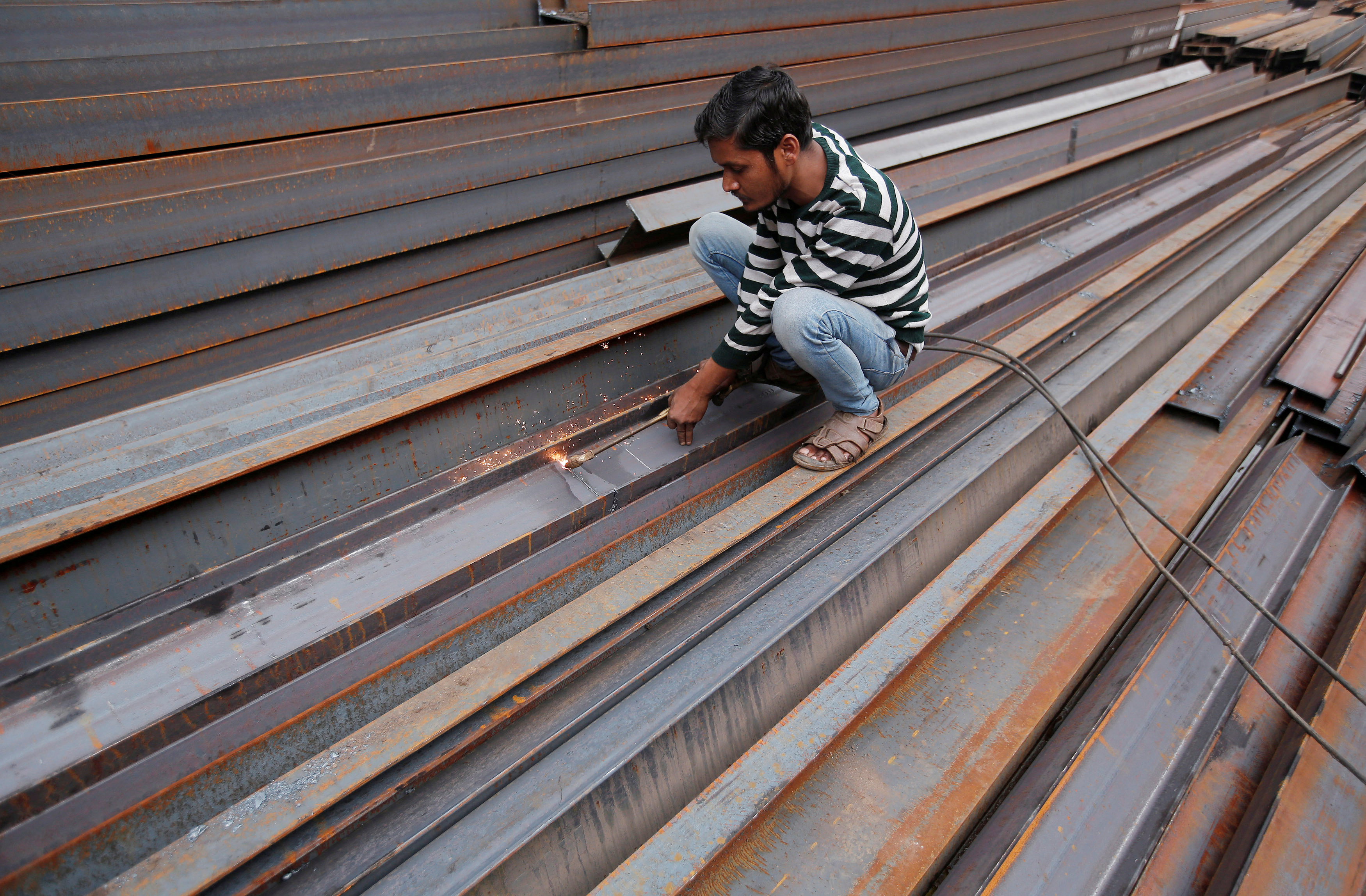 A worker cuts iron rods outside a workshop at an iron and steel market in an industrial area in New Delhi