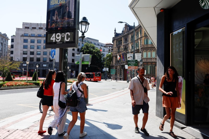 People walk past a temperature panel reading 49 degrees celsius (120 Fahrenheit) in Bilbao