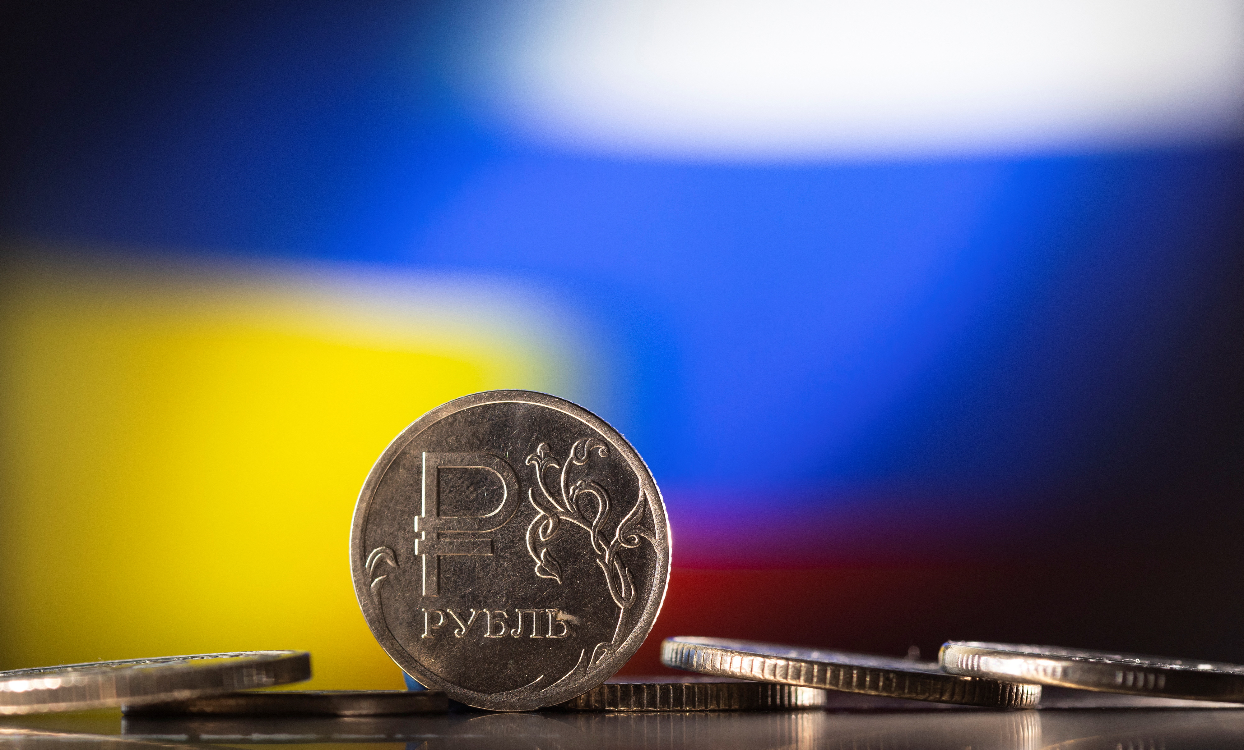 Illustration shows Russian Rouble coins are seen in front of displayed Ukrainian's and Russia's flag colours