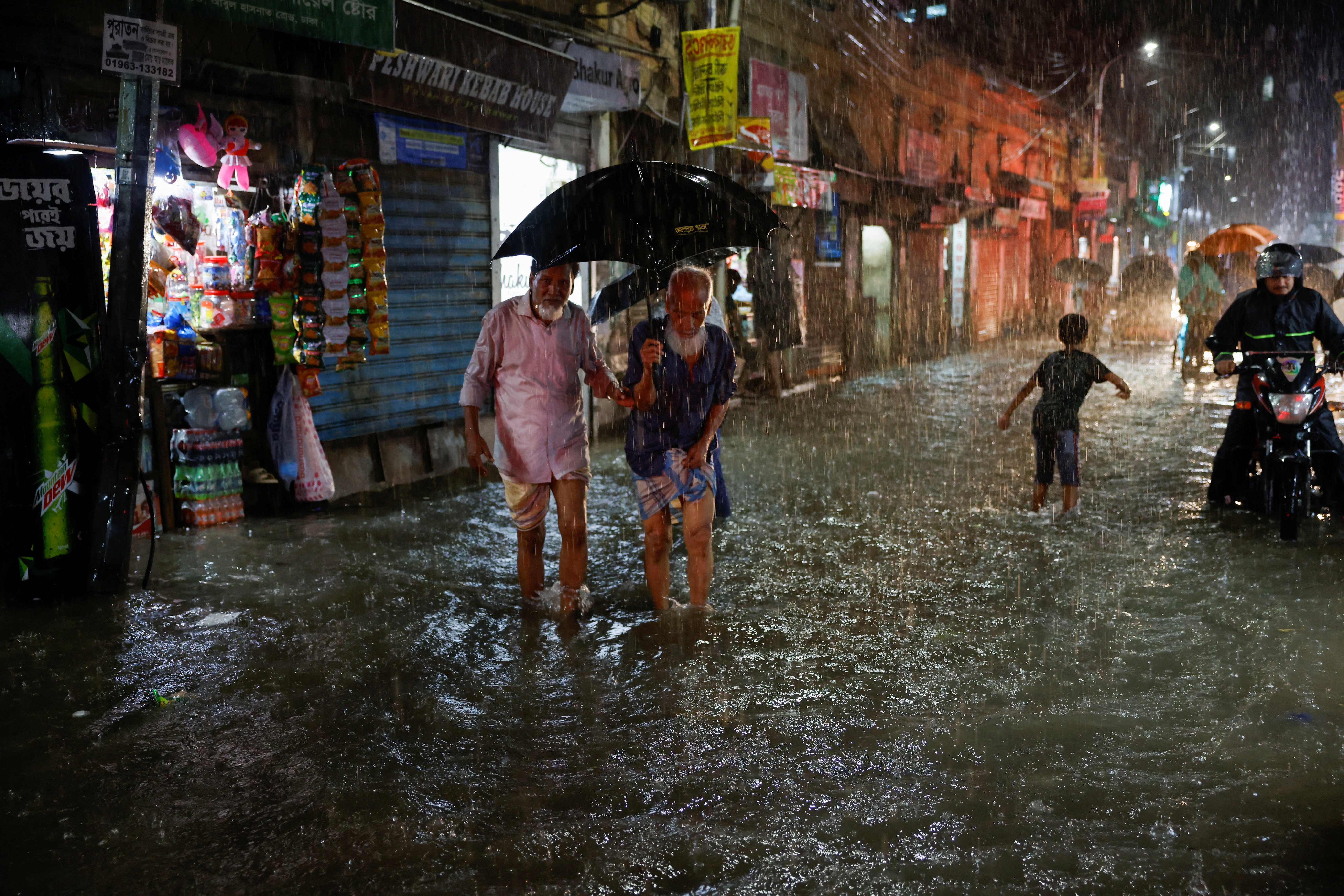 People wade through a flooded street amid continuous rain before the Cyclone Sitrang hits in Dhaka
