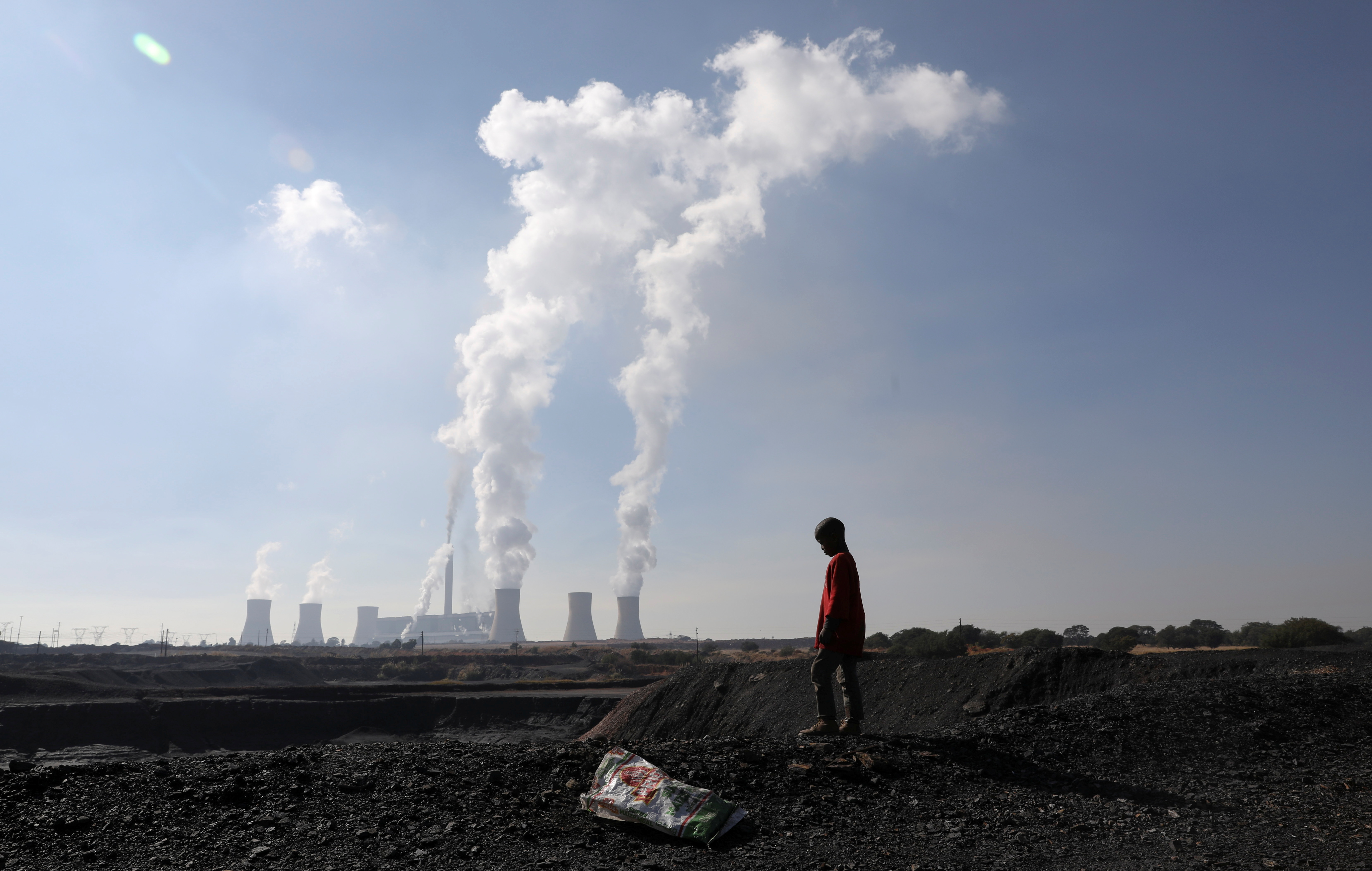 A child collecting chunks of coal looks on at a colliery while smoke rises from the Duvha coal-based power station owned by state power utility Eskom, in Emalahleni, in Mpumalanga province, South Africa, June 2, 2021. REUTERS/Siphiwe Sibeko