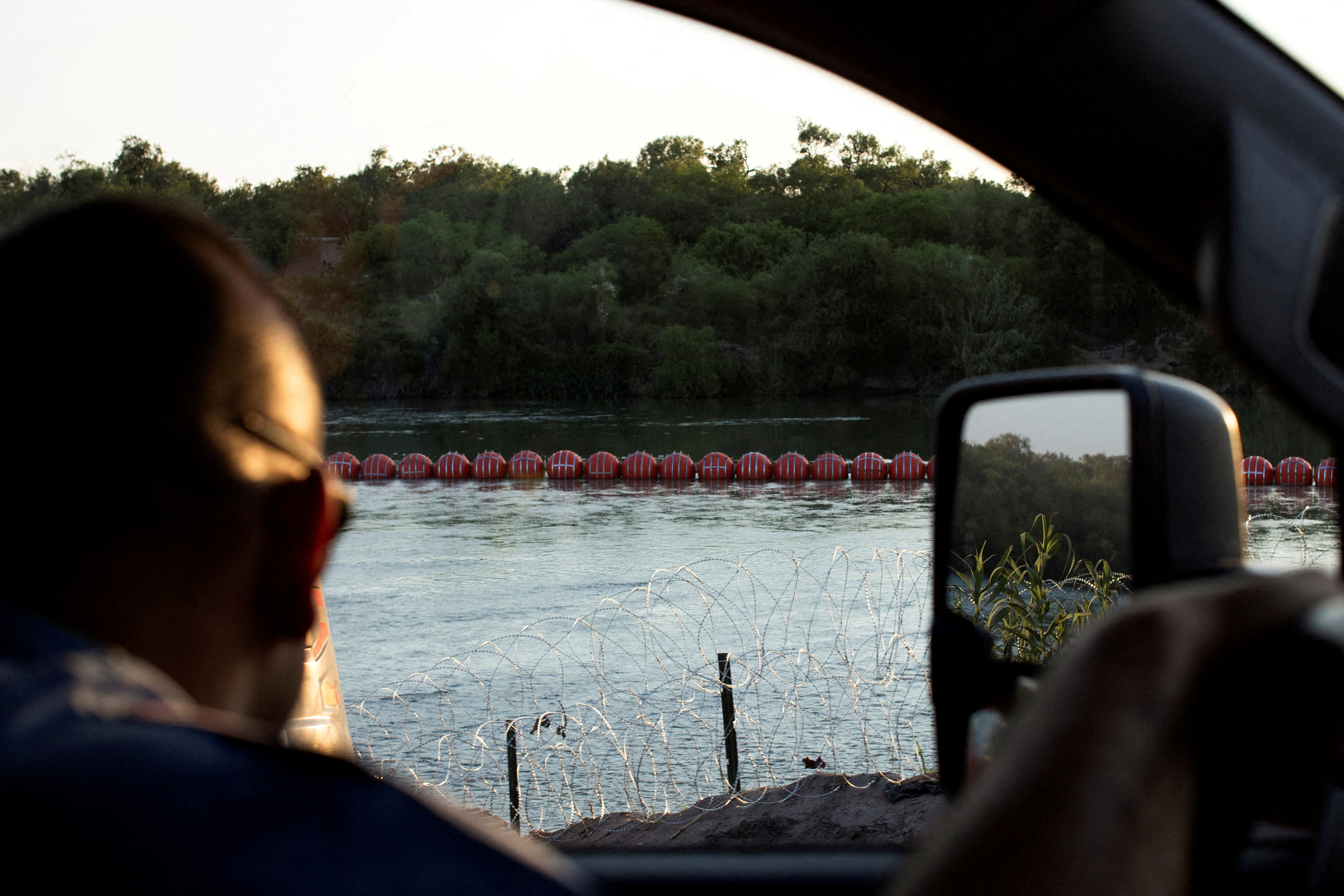 Station One Company C, Captain Luis Gonzalez, looks out at an unfinished orange buoy barrier placed in the Rio Grande River in response to migrants crossing the river, near Eagle Pass,