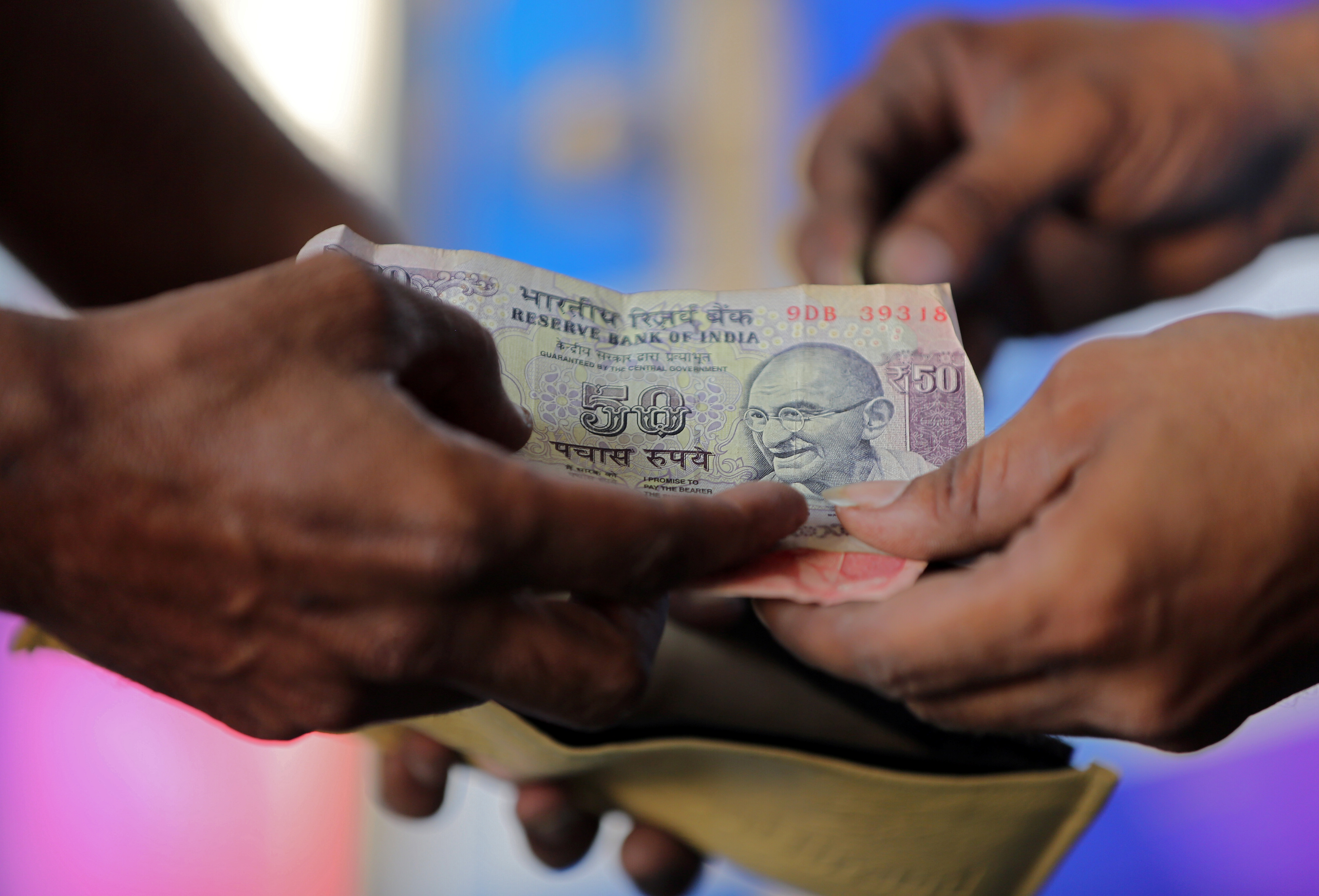 A customer hands a 50-Indian rupee note to an attendant at a fuel station in Ahmedabad