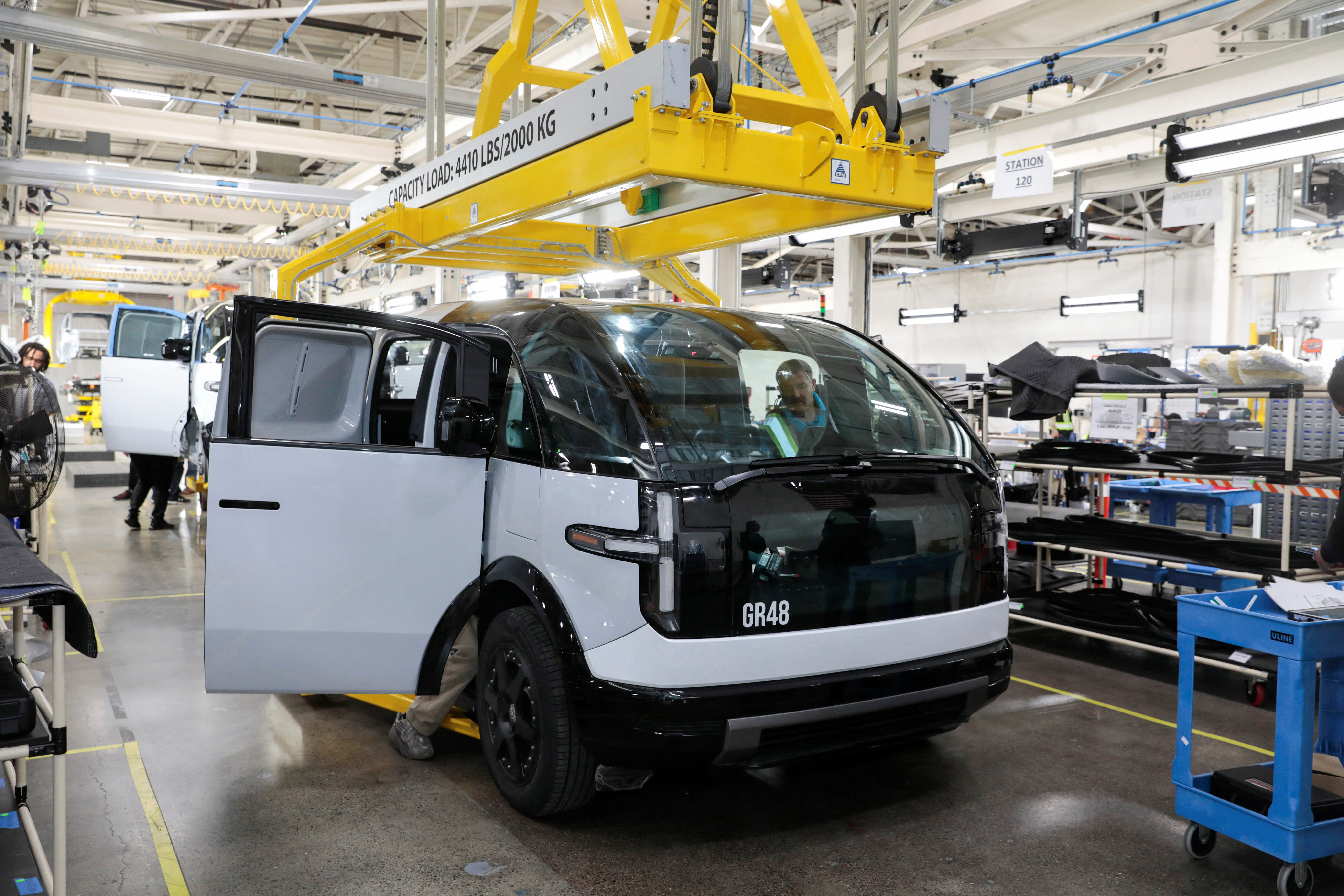 Production employees work on a Canoo electric vehicle at a manufacturing site