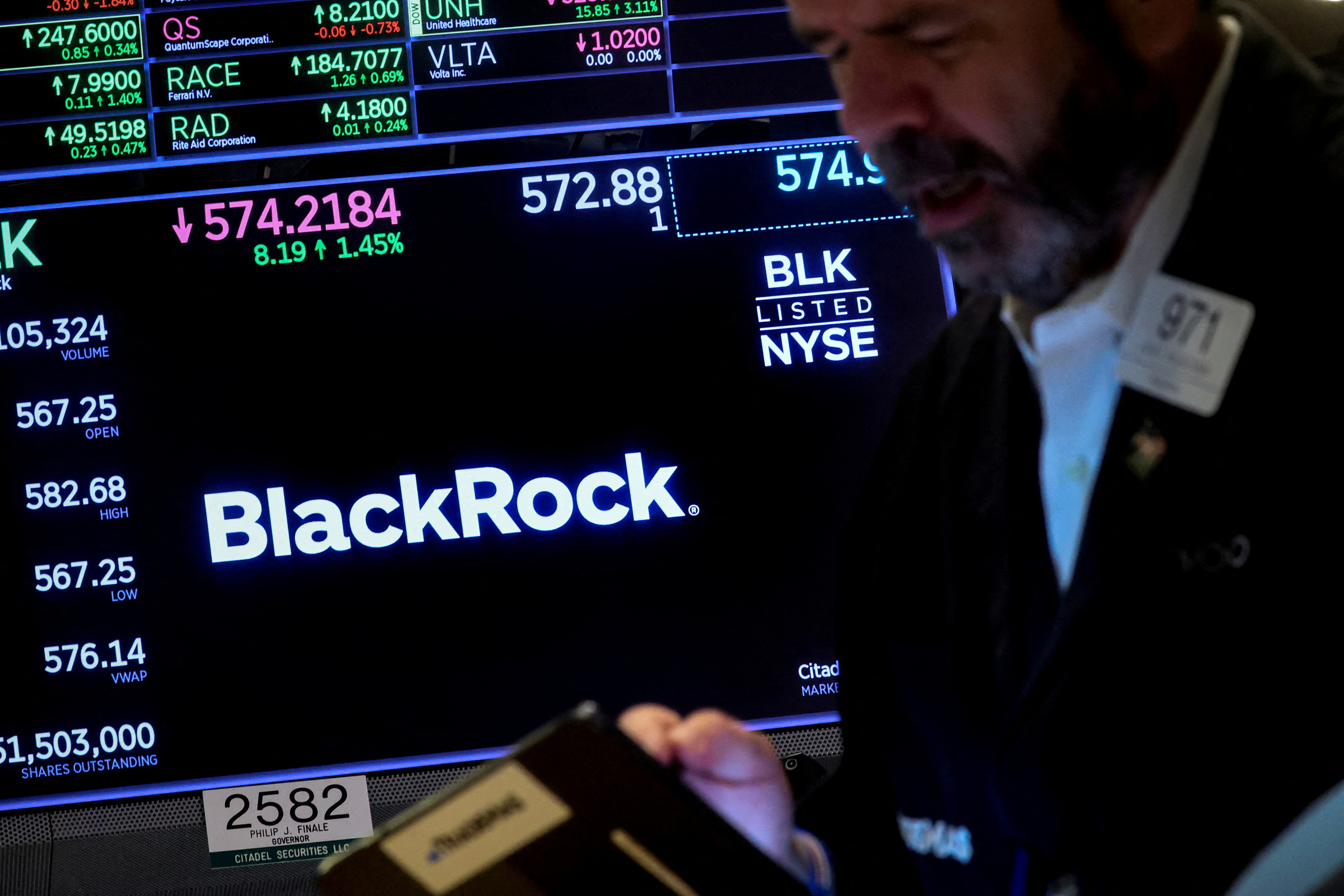 A trader works as a screen displays the trading information for BlackRock on the floor of the NYSE in New York