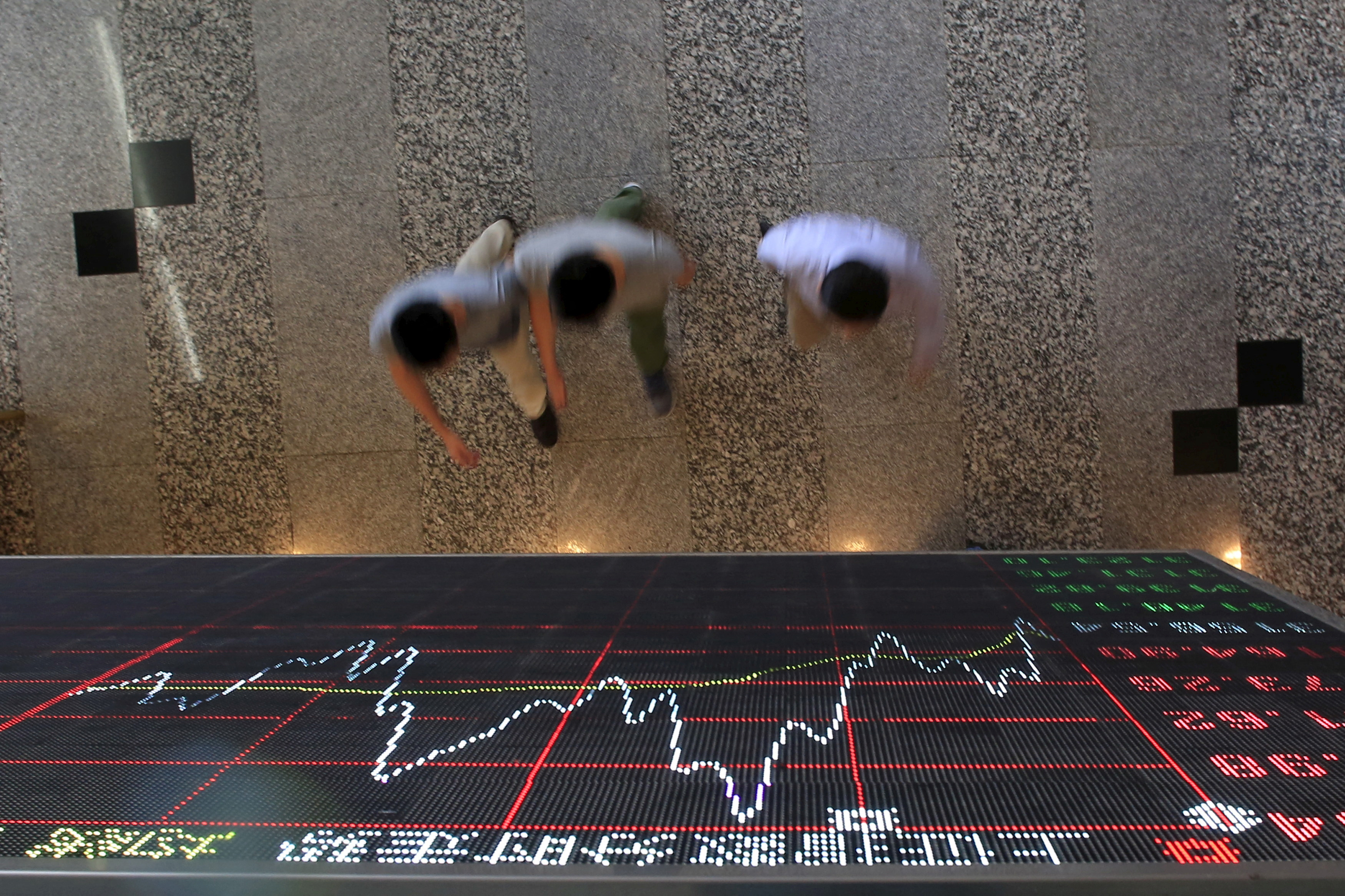 People walk under an electronic board showing stock information at the Shanghai Stock Exchange in Lujiazui Financial Area in Shanghai