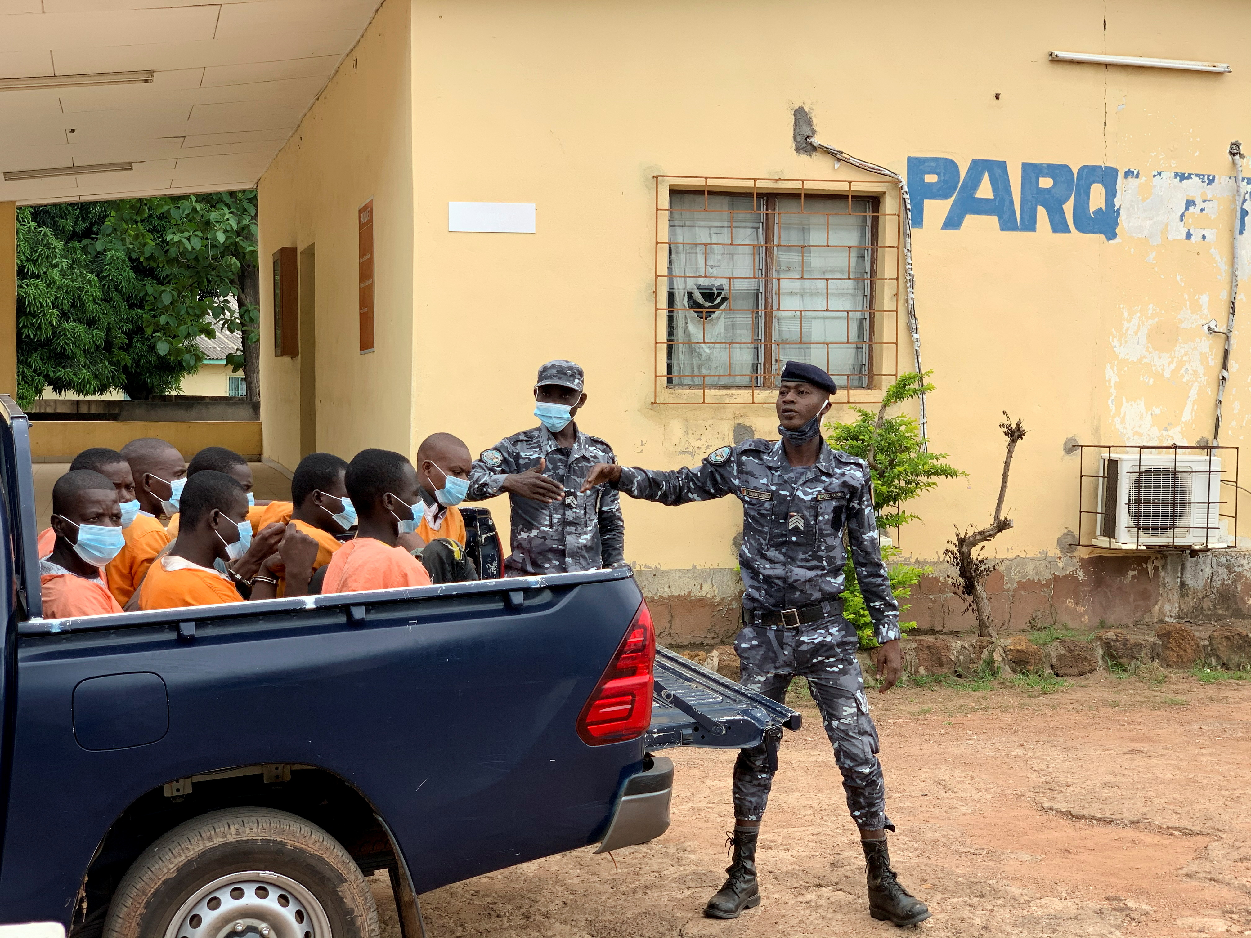 Police officers escort a group of men accused of child trafficking at a court in Bouna