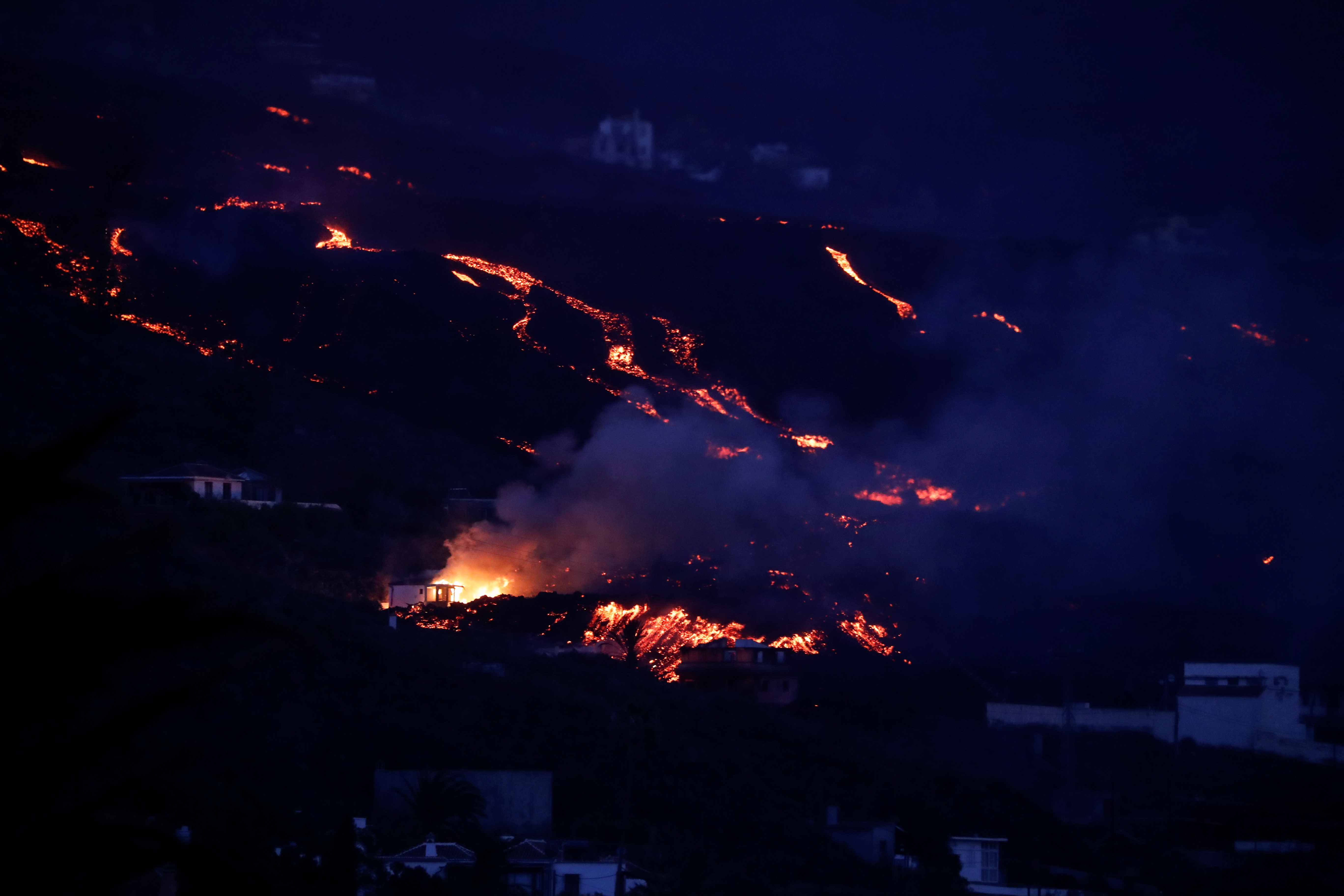 Tajuya, İspaniya, 23 oktyabr 2021-ci il tarixindən göründüyü kimi, vulkan La Palma Kanar adasında püskürməyə davam edərkən Cumbre Vieja vulkanından lava yanan evin yanından enişlə aşağı axır. REUTERS/Susana Vera