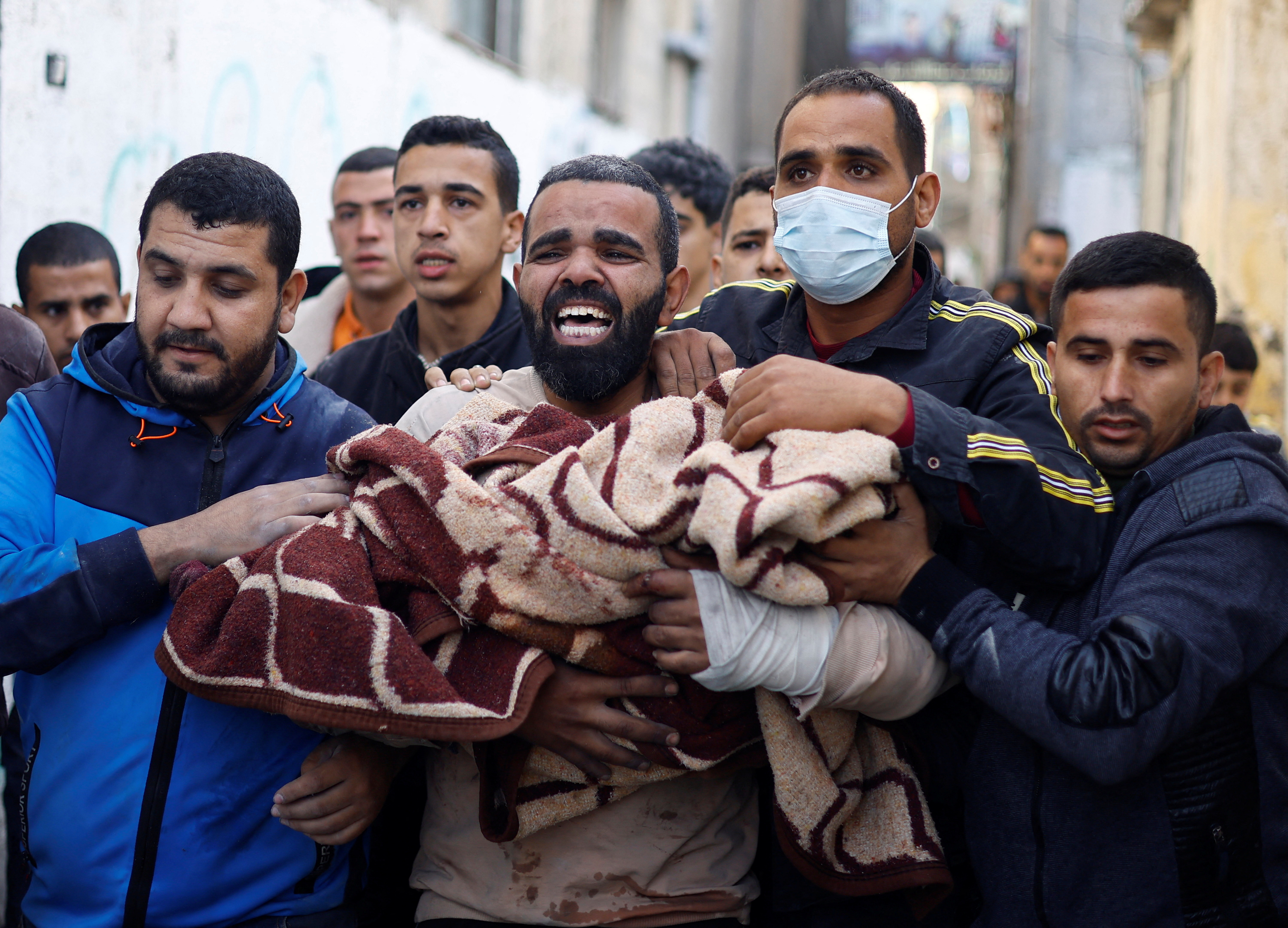 A Palestinian man carries a child casualty at the site of Israeli strikes on houses, in Rafah