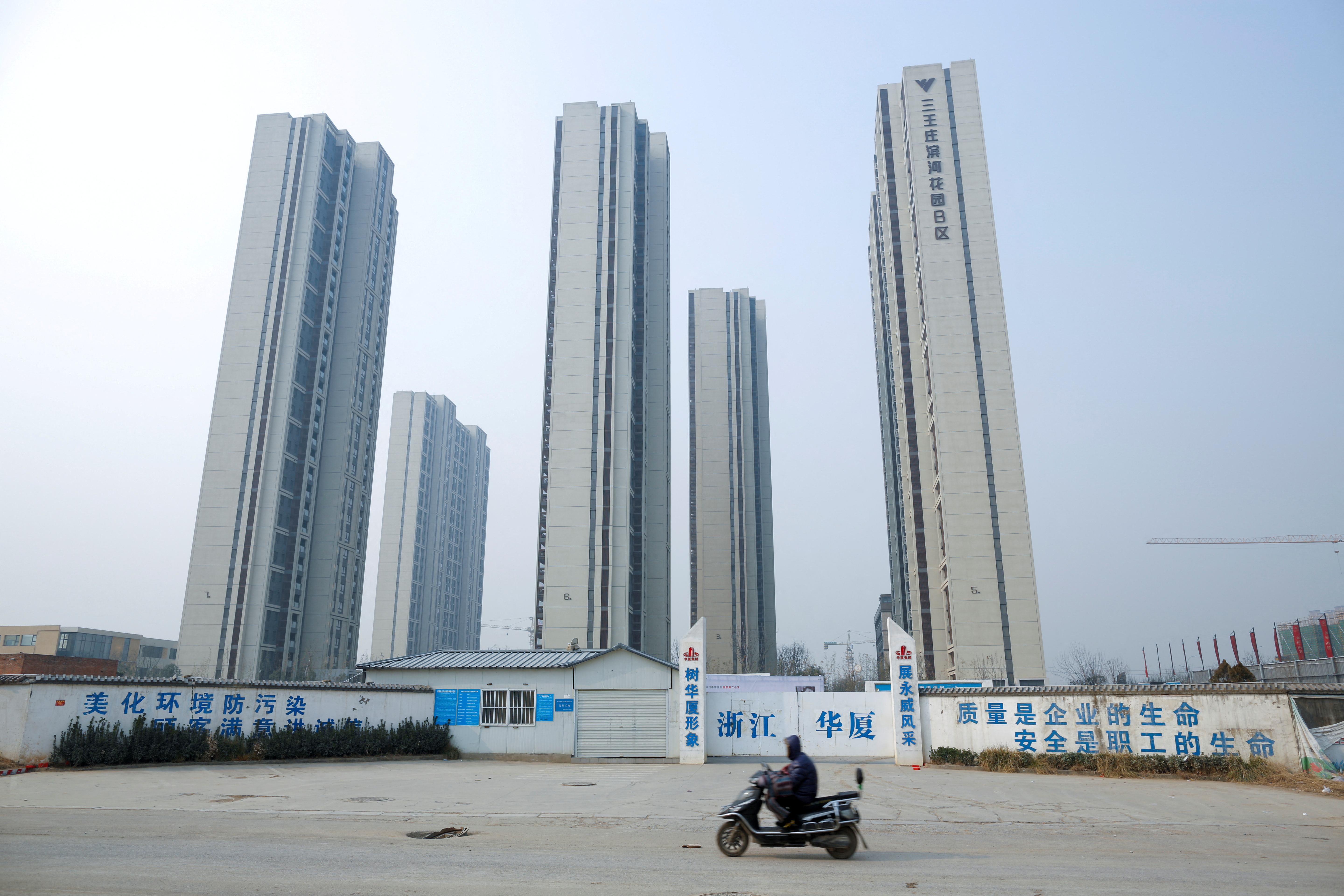 A man rides a scooter past apartment highrises that are under construction near the new stadium in Zhengzhou