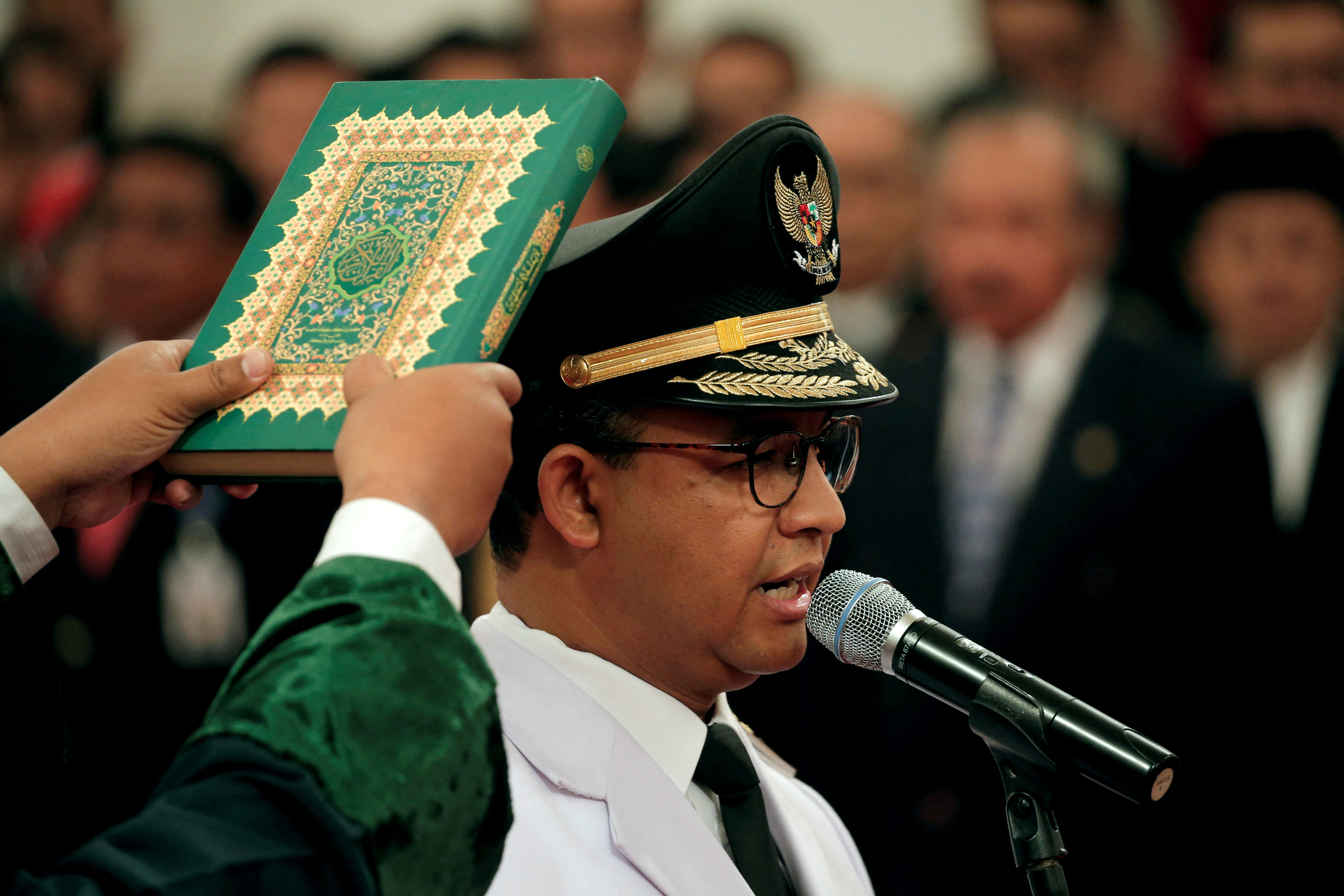 A man holds a Koran as Jakarta Governor Anies Baswedan stands during a swearing-in ceremony at the Presidential Palace in Jakarta