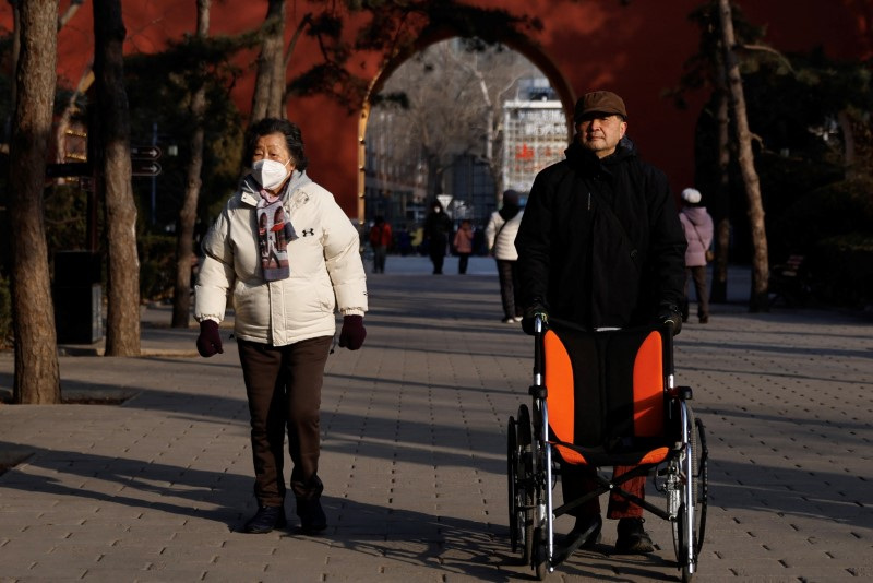 An elderly man pushes a wheelchair as he walks at a park in Beijing