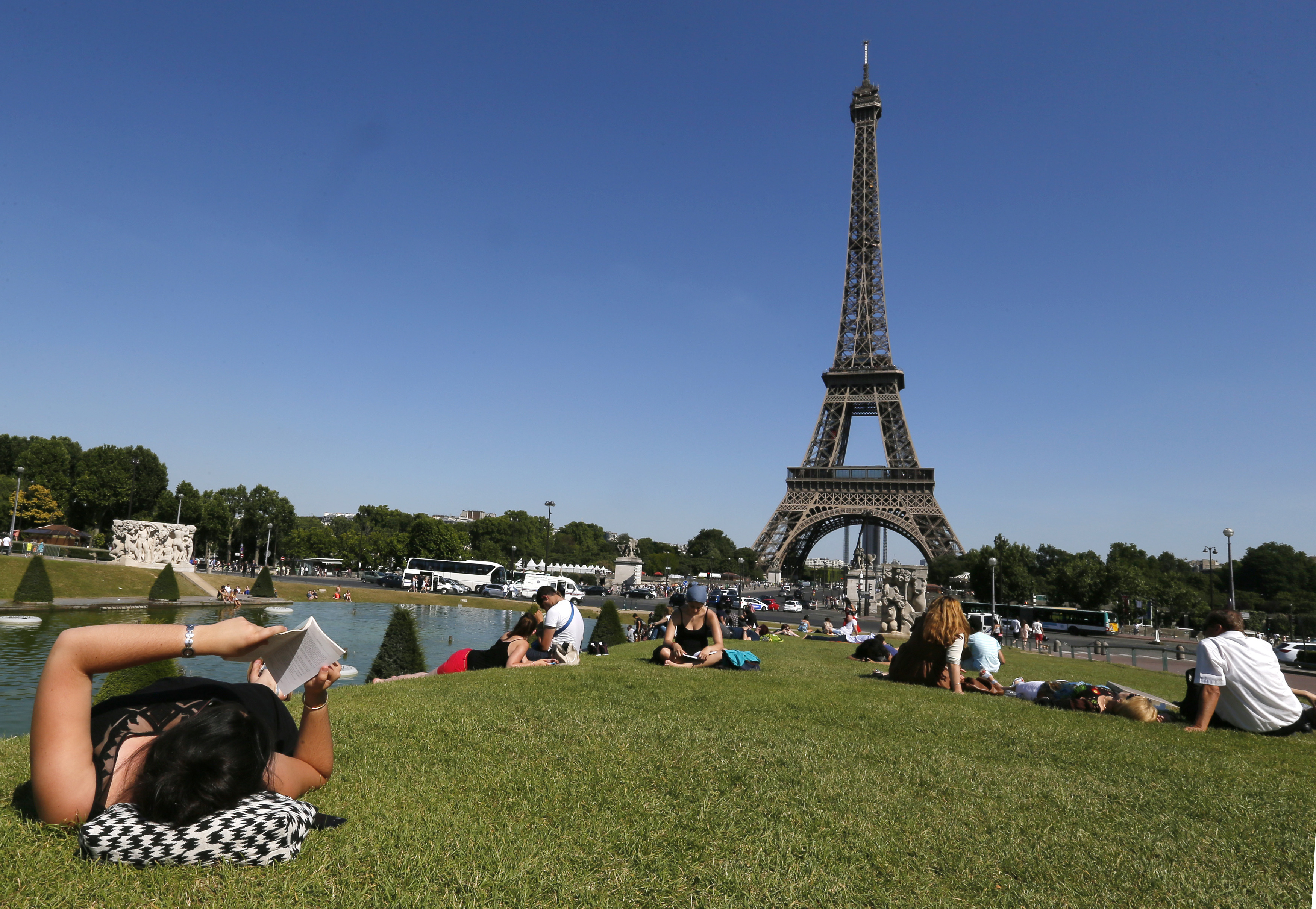 A woman reads a book as she rests in a public garden near the Eiffel Tower on a hot summer day in Paris